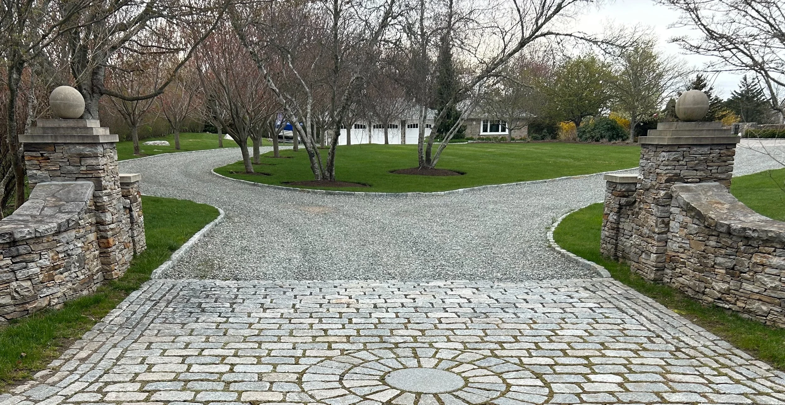 Beautiful pebble driveway with stone apron by GrandScapes