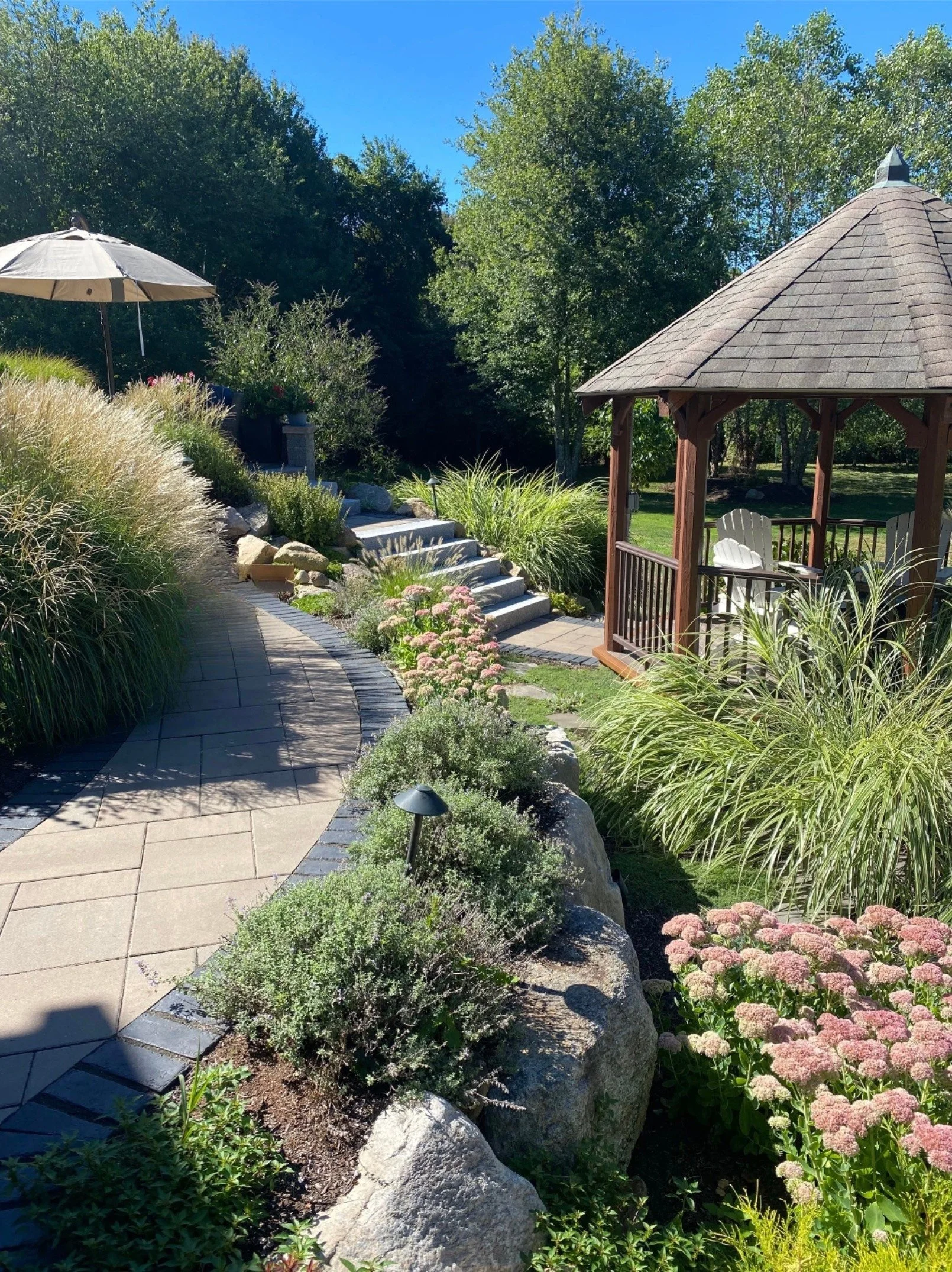 Stone patio walkway with beautiful plantings and wooden gazebo