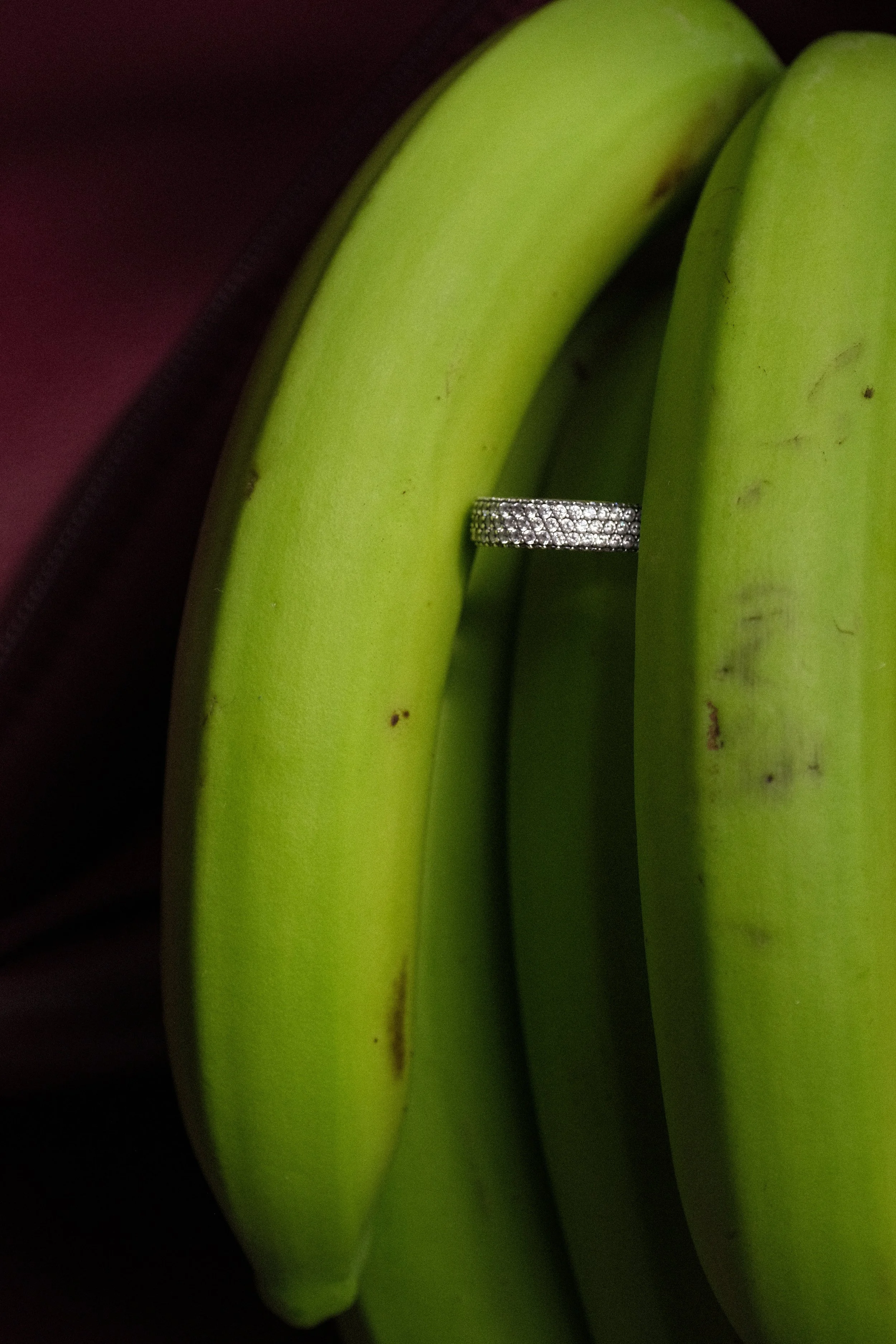 A cluster of green bananas with a diamond ring placed between two bananas.