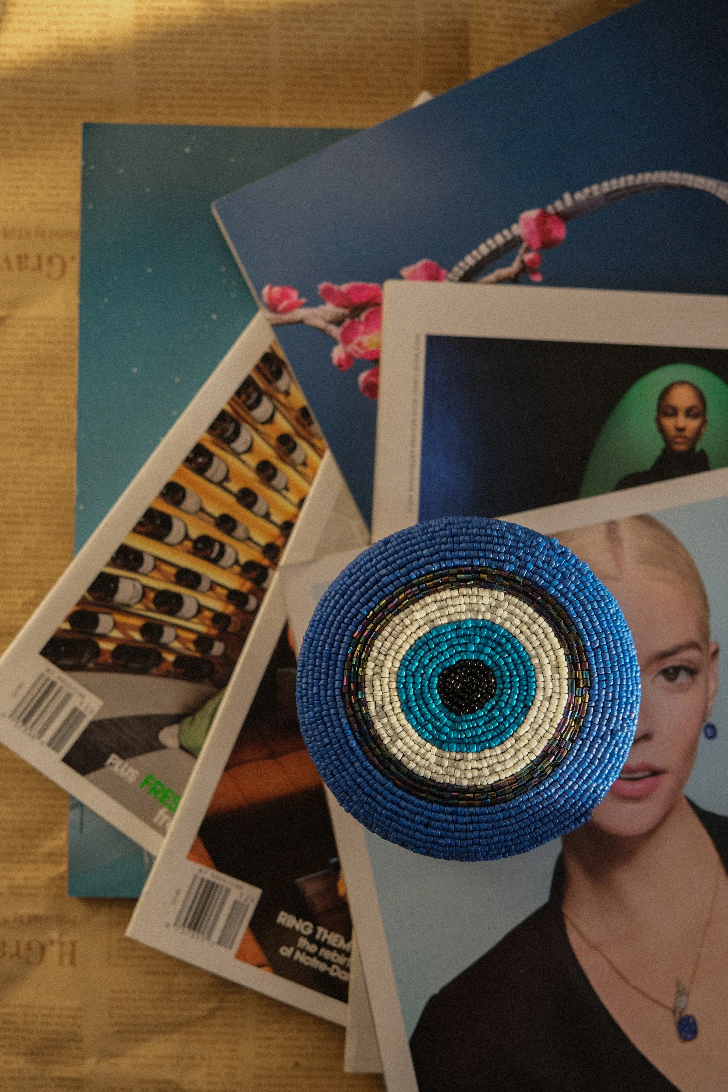 Top view of a beaded peace sign ring placed on magazines, with magazines and a newspaper underneath.