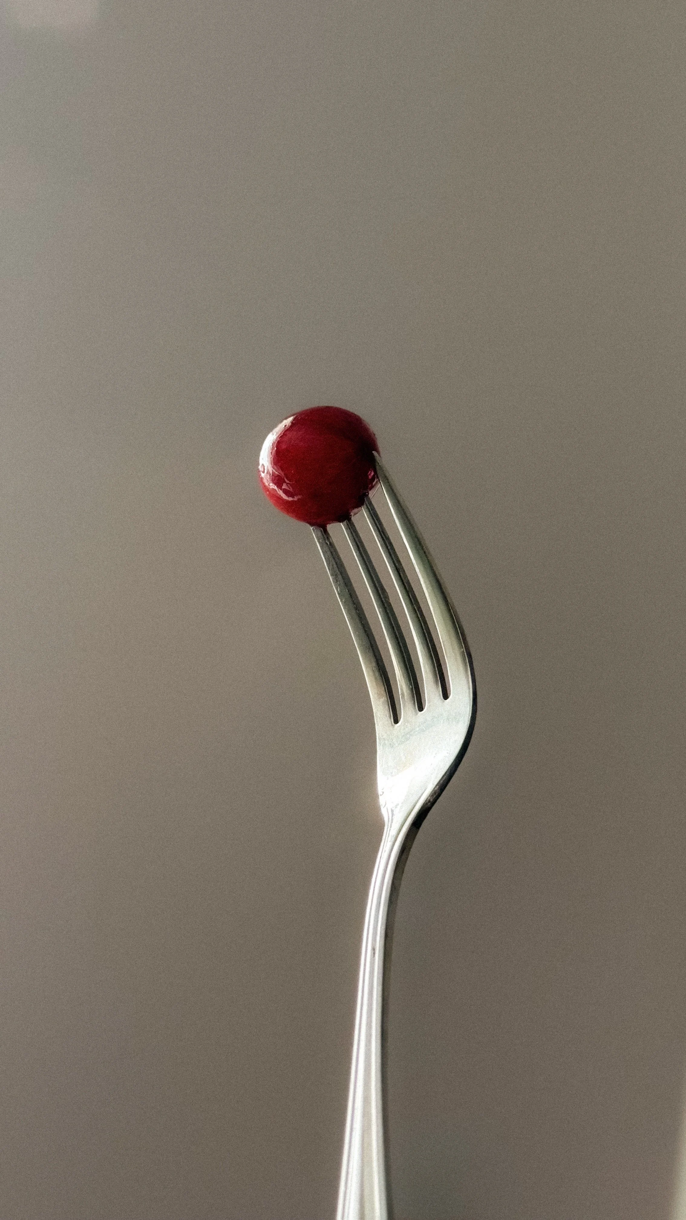 A silver fork holding a single red cherry tomato against a neutral background.