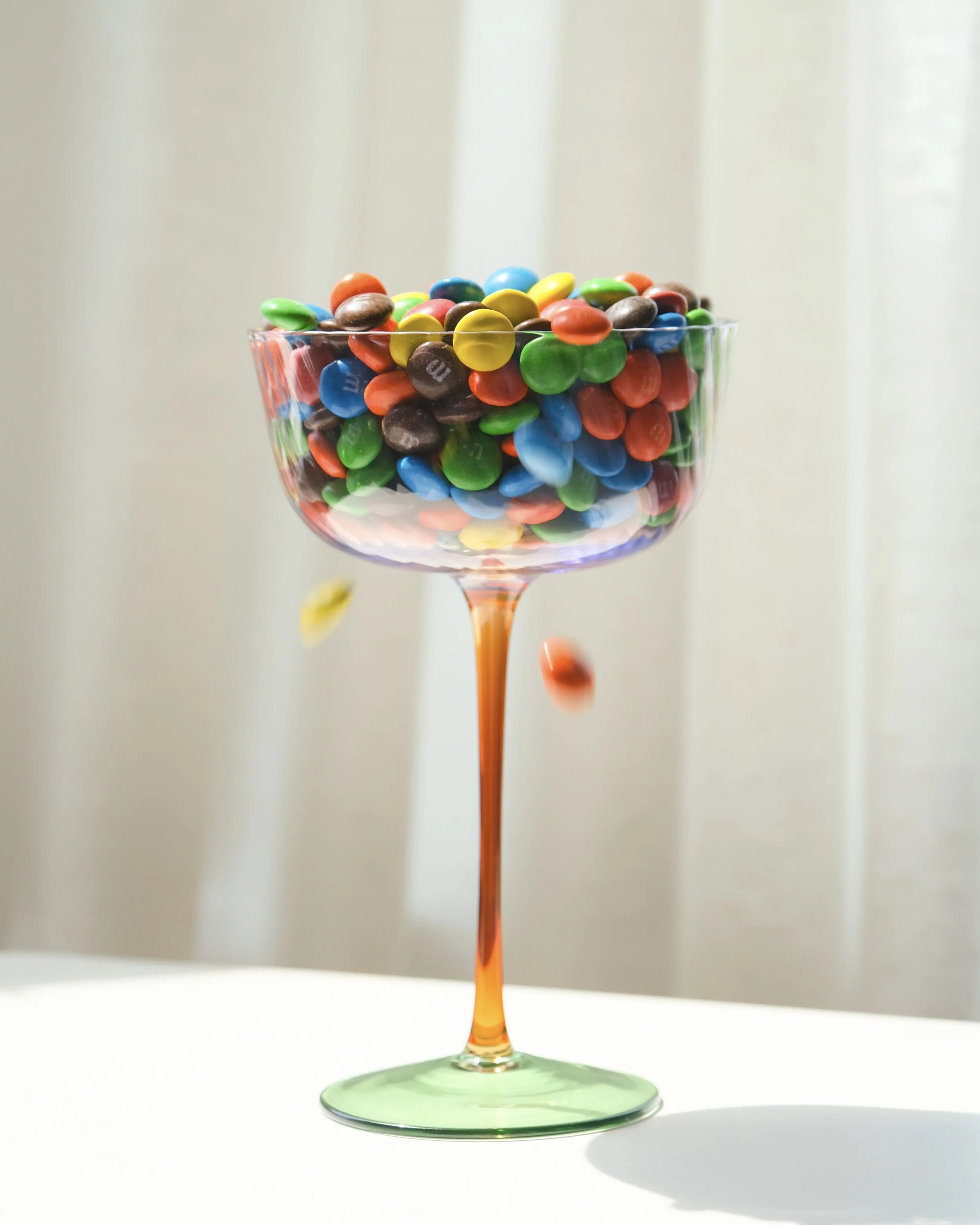 Colorful M&M candies in a glass bowl with some spilling out.