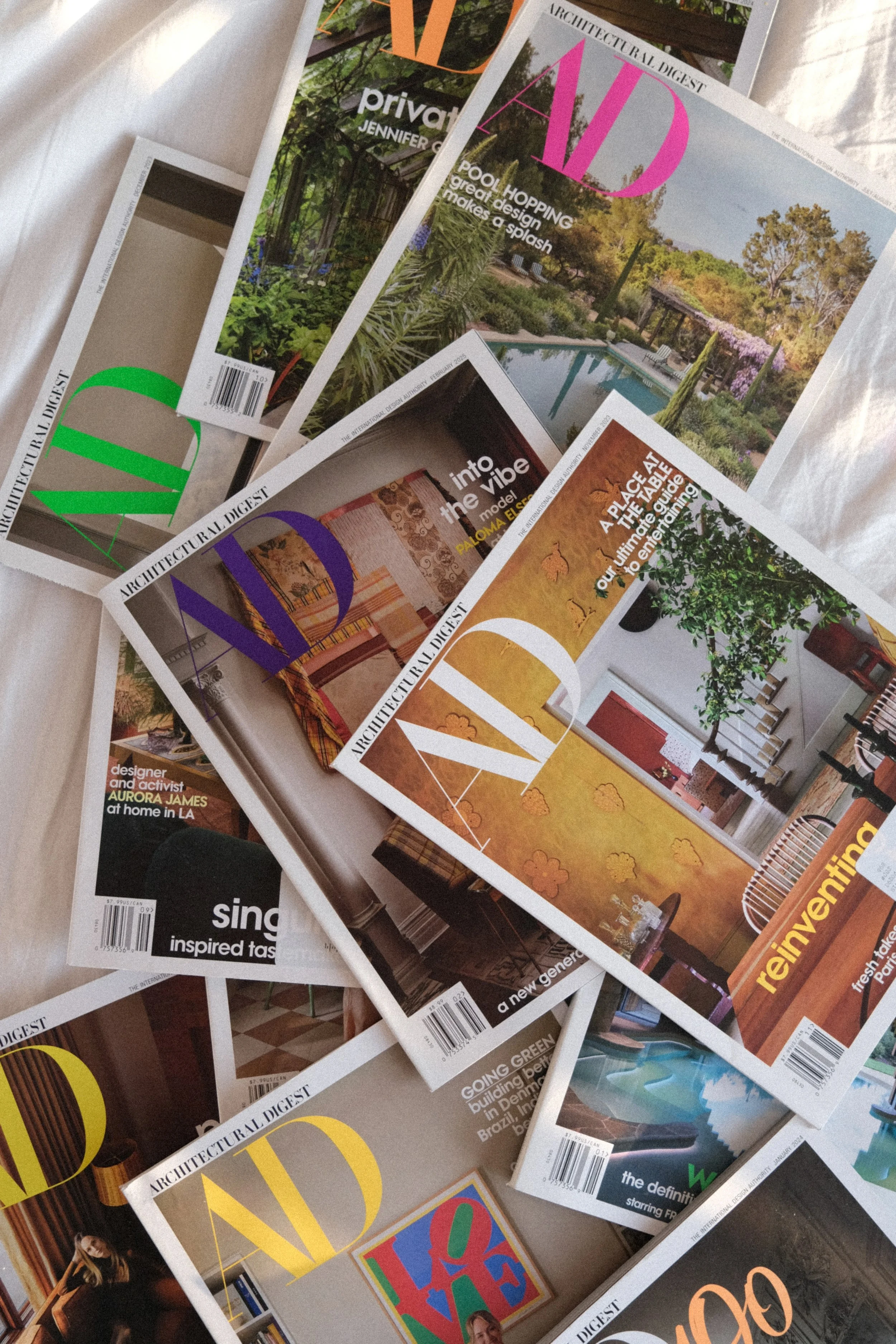Multiple issues of Architectural Digest magazine scattered on a surface, with various cover images including interior design, outdoor landscapes, and artwork.