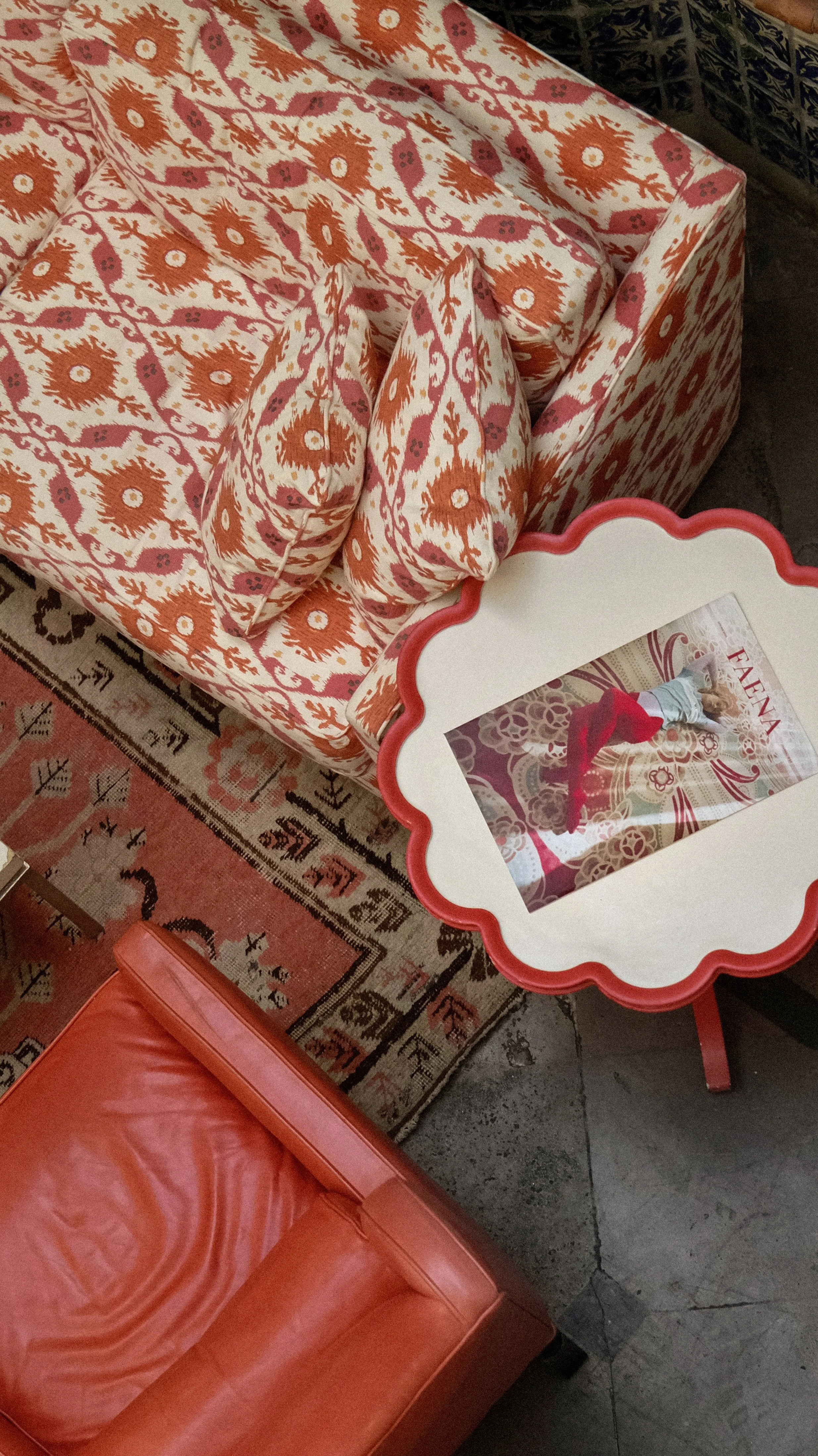 A decorative table with a children's birthday party setup, showing a framed photo of a child performing a handstand on a patterned background, a large fabric armchair with orange and white floral patterns, a pink and white rug, and an orange cushione