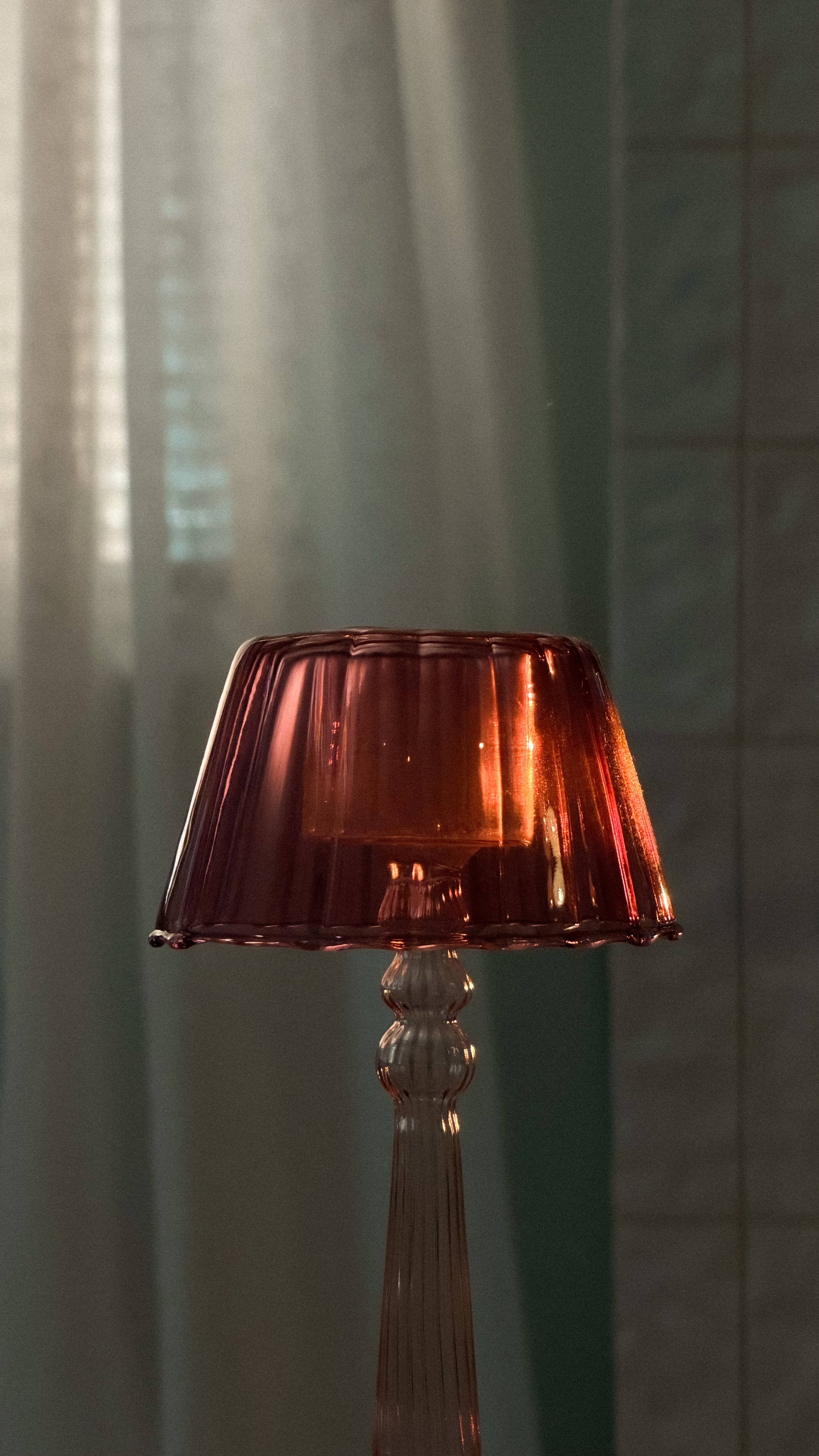 A tall lamp with a semi-transparent brownish-red lampshade and a glass base, lit in a softly lit room.