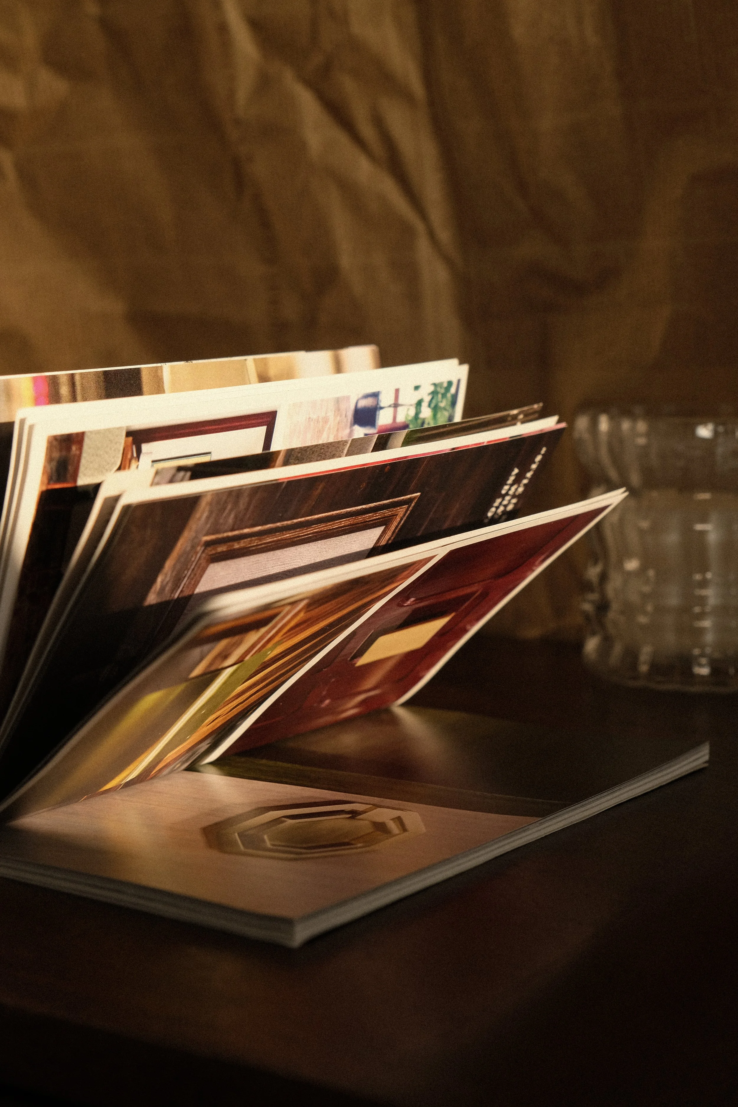 Open magazine with interior room decor images on a dark wooden table, with a glass of water in the background.