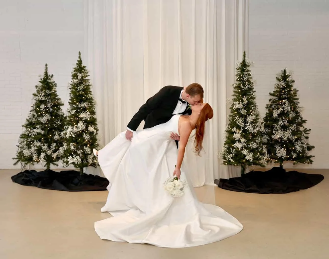 Picture taken by Michigan photographer during wedding that live wedding painter painted from.  Shows bride and groom in a dip kiss between two christmas trees