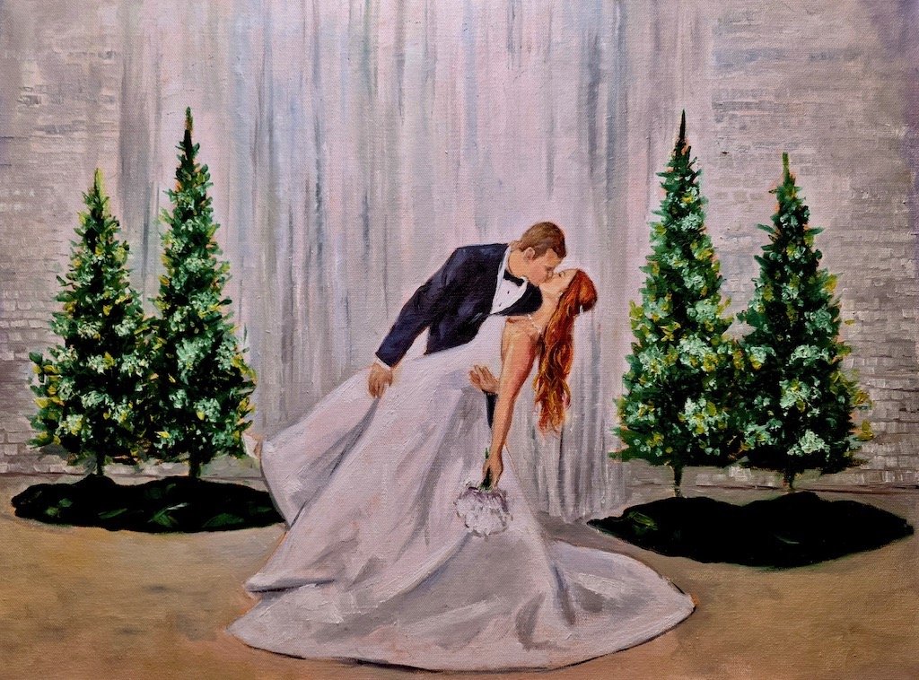 Live wedding painting of a wedding couple sharing a kiss, with the bride holding a bouquet. Two decorated Christmas trees are on either side in front of a gray curtain backdrop.