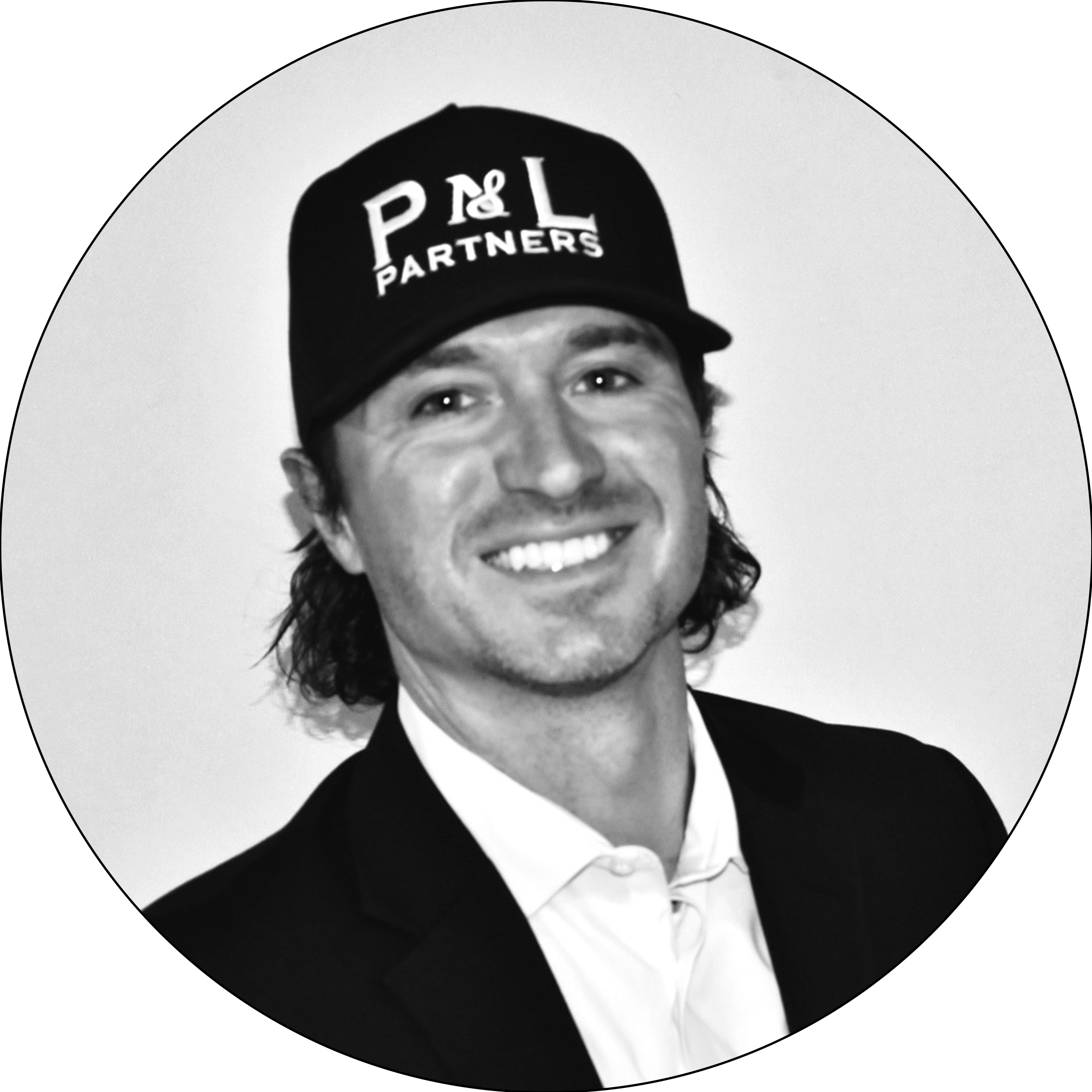 A black and white photo of a smiling woman wearing a black jacket, white shirt with ruffled collar, and a black baseball cap with the logo "P & L Partners."