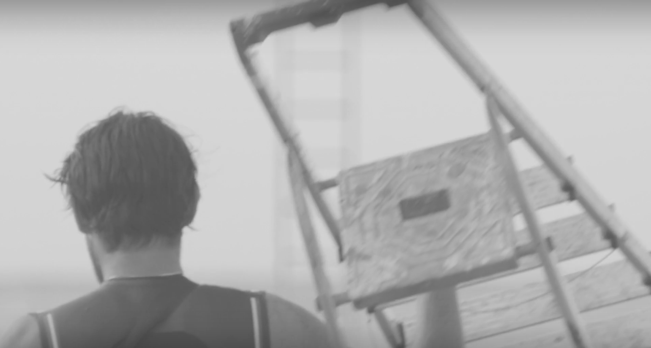 A person with short hair seen from behind on a beach, near a wooden ladder and a lifeguard chair.