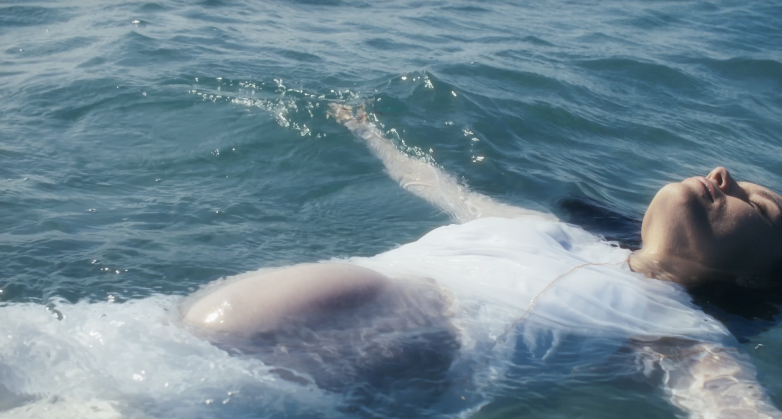 Person lying on their back in the ocean, floating peacefully, with calm blue water surrounding them.