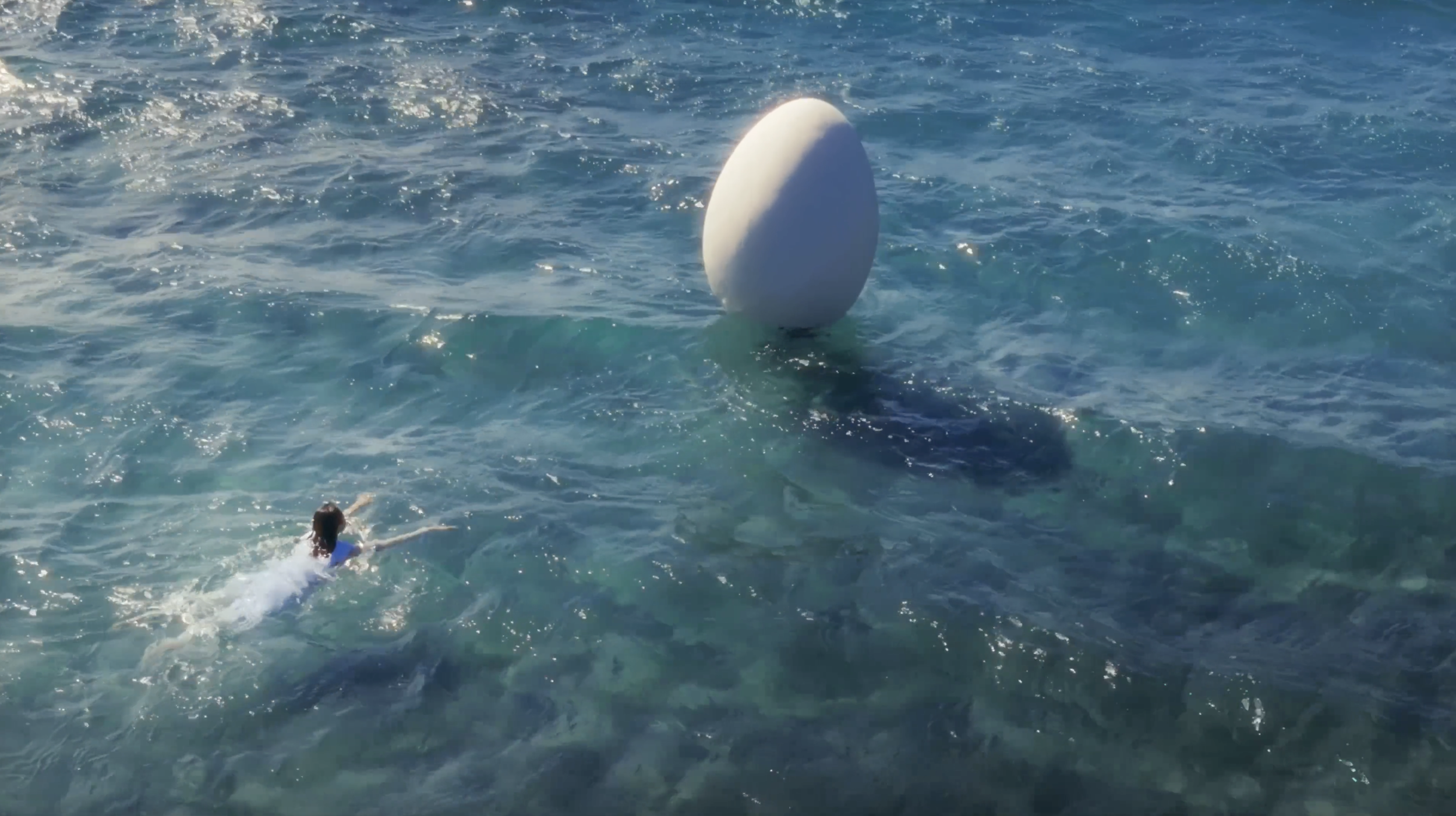 A woman swimming in the ocean with a large white egg-shaped object floating nearby.