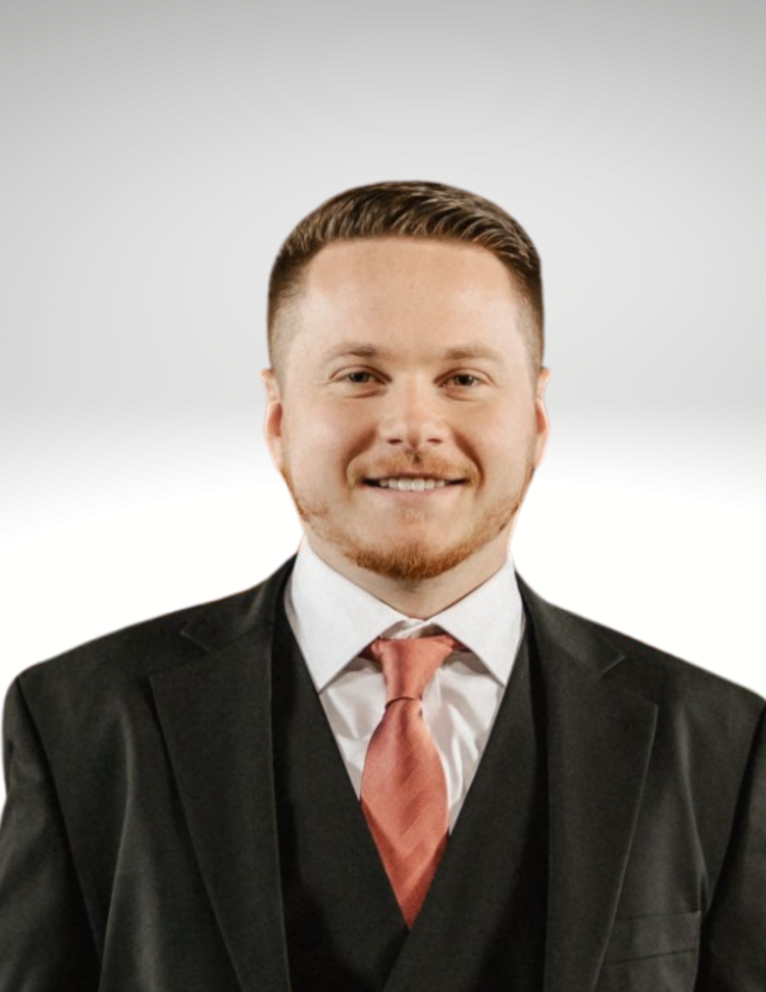 A man in a suit smiling, wearing a white shirt, red tie, and dark blazer, against a plain light gray background.