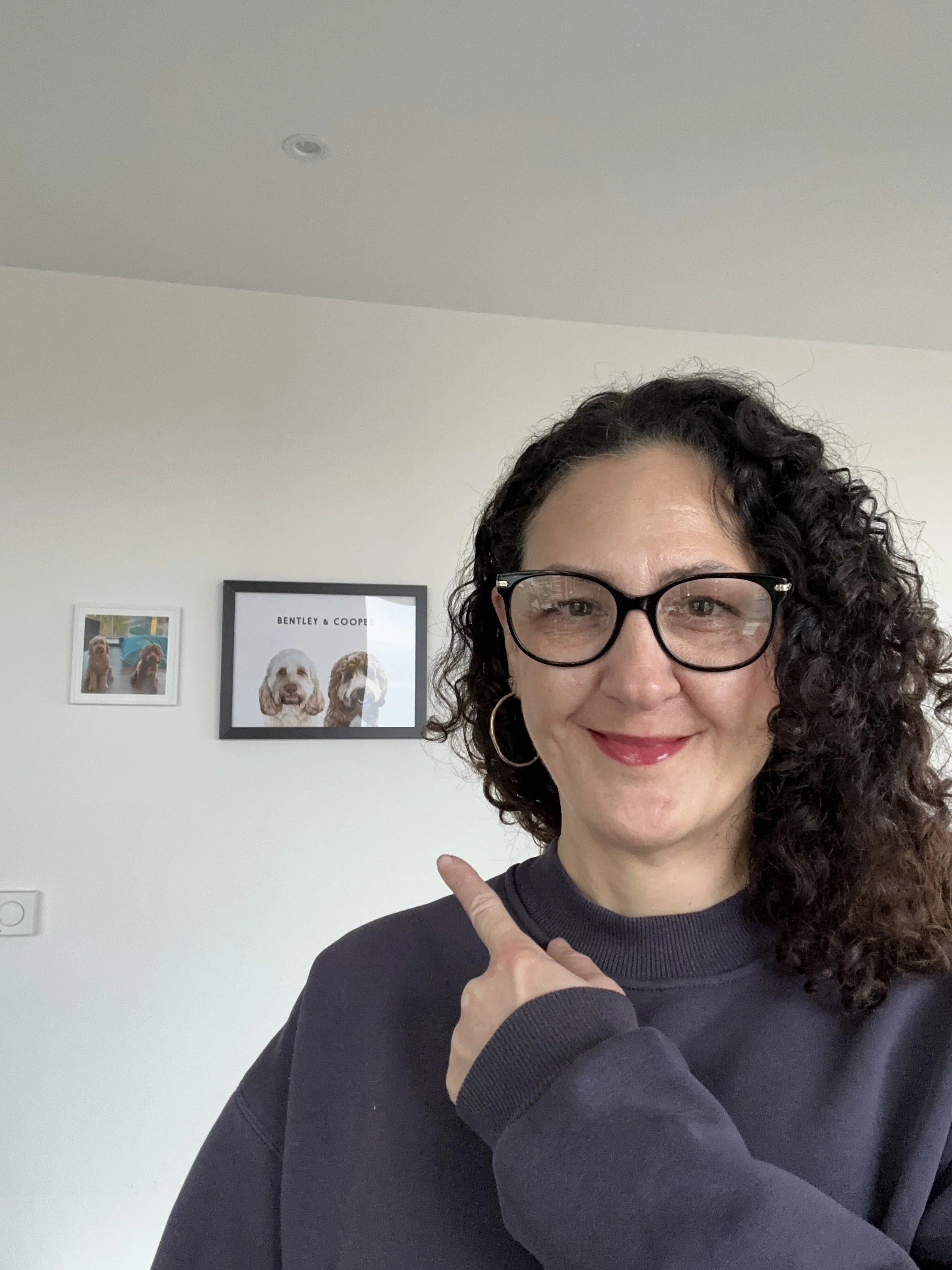 Izzy Raffi, co-founder of flüf, smiling in front of framed photos of her dogs Bentley and Cooper.
