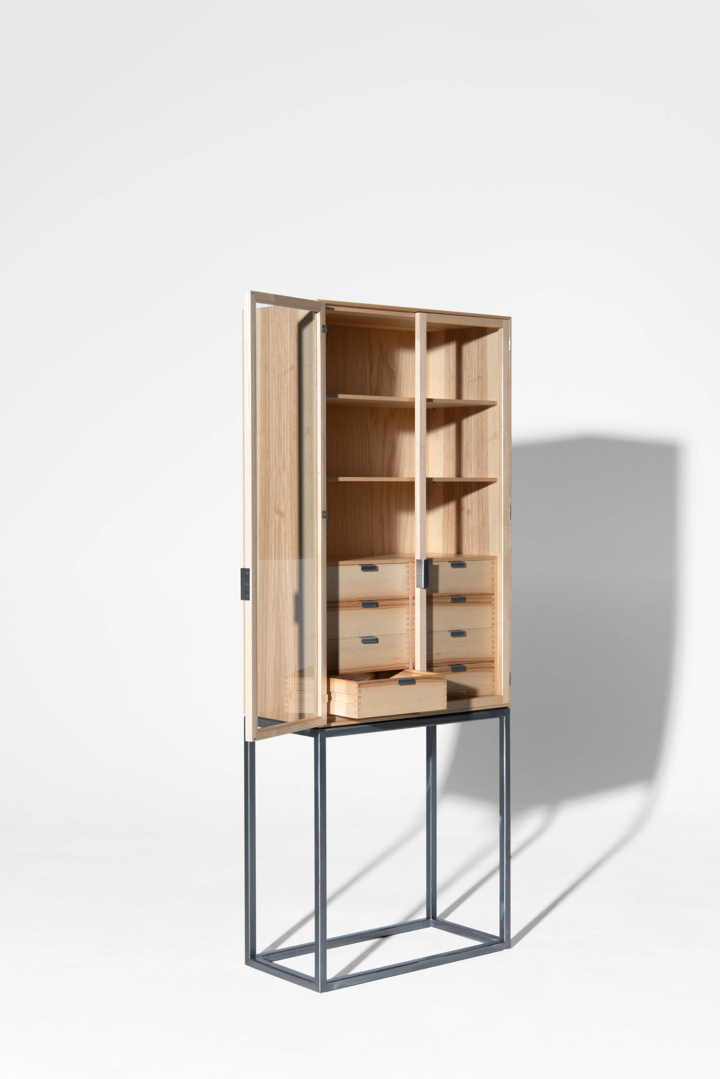 Ein leicht geöffnetes Holzzimmer mit Schubladen und Regalen auf einem metallischen Ständer, vor einem weißen Hintergrund.