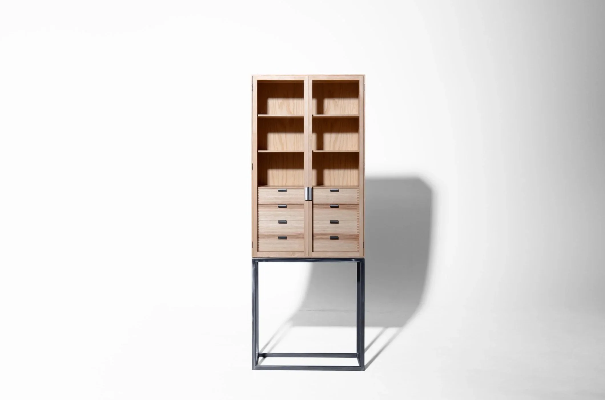 Ein holzener Schrank mit mehreren Fächern und Schubladen, auf einem schwarzen Metallrahmen, vor einer weißen Wand