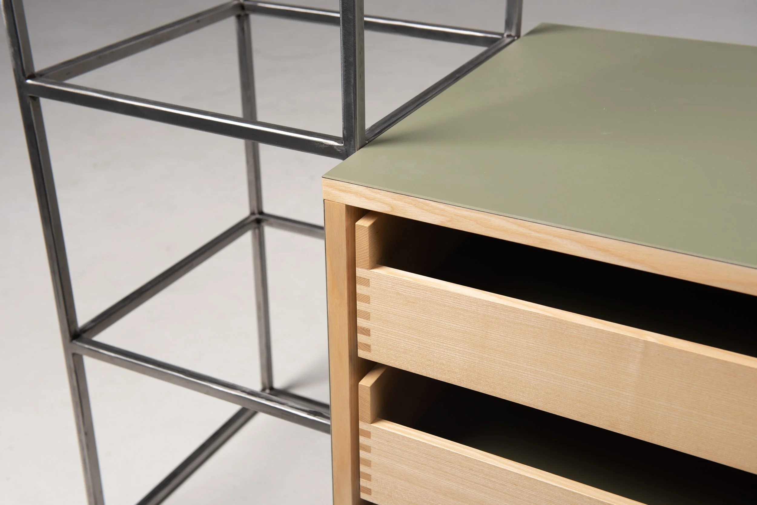 Nahaufnahme von zwei unterschiedlichen Möbelstücken, einem metallischen Regal und einem Holzkommode, mit Fokus auf die Details und Materialien.