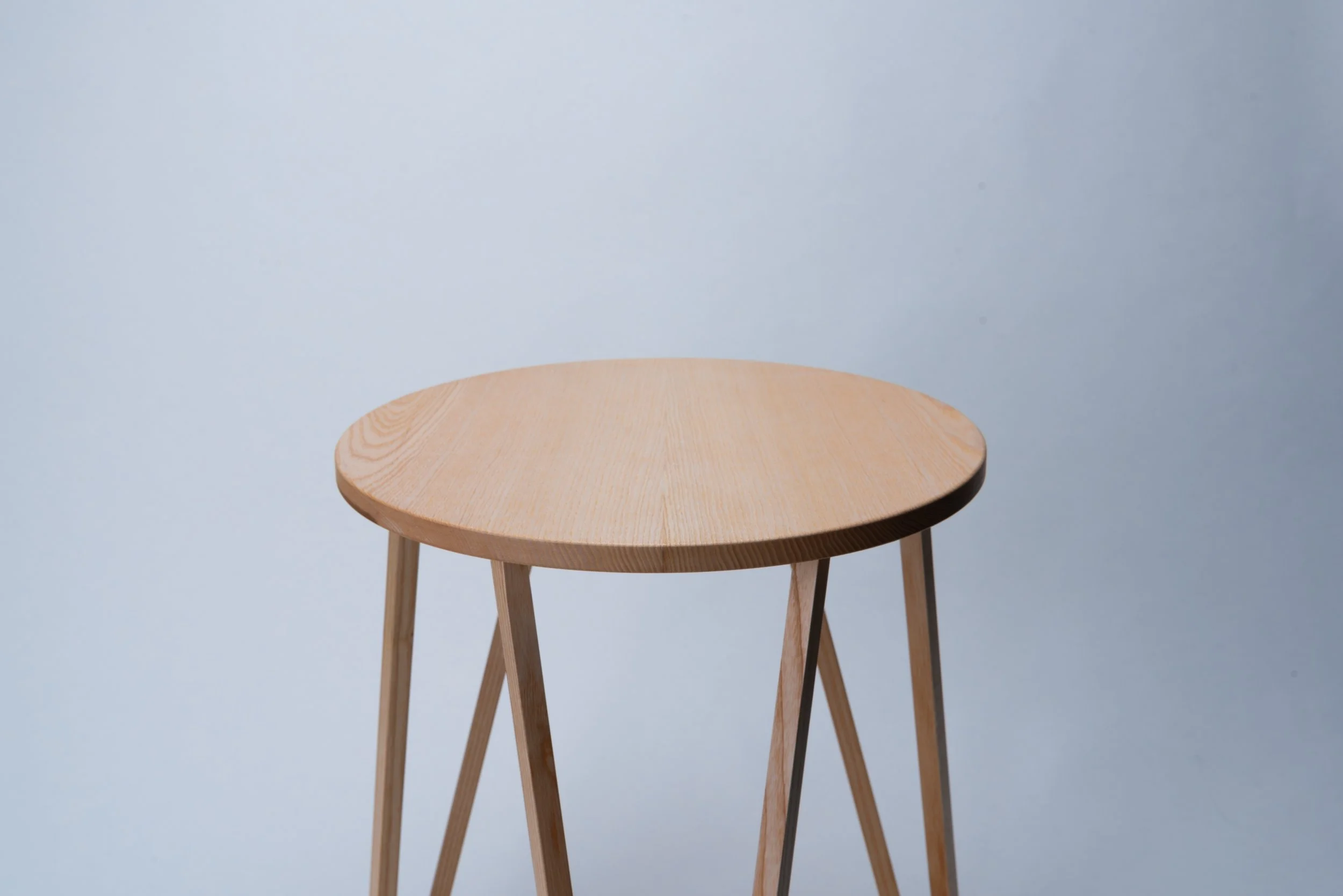 Hölzerner Stuhl mit runder Sitzfläche vor hellem Hintergrund.