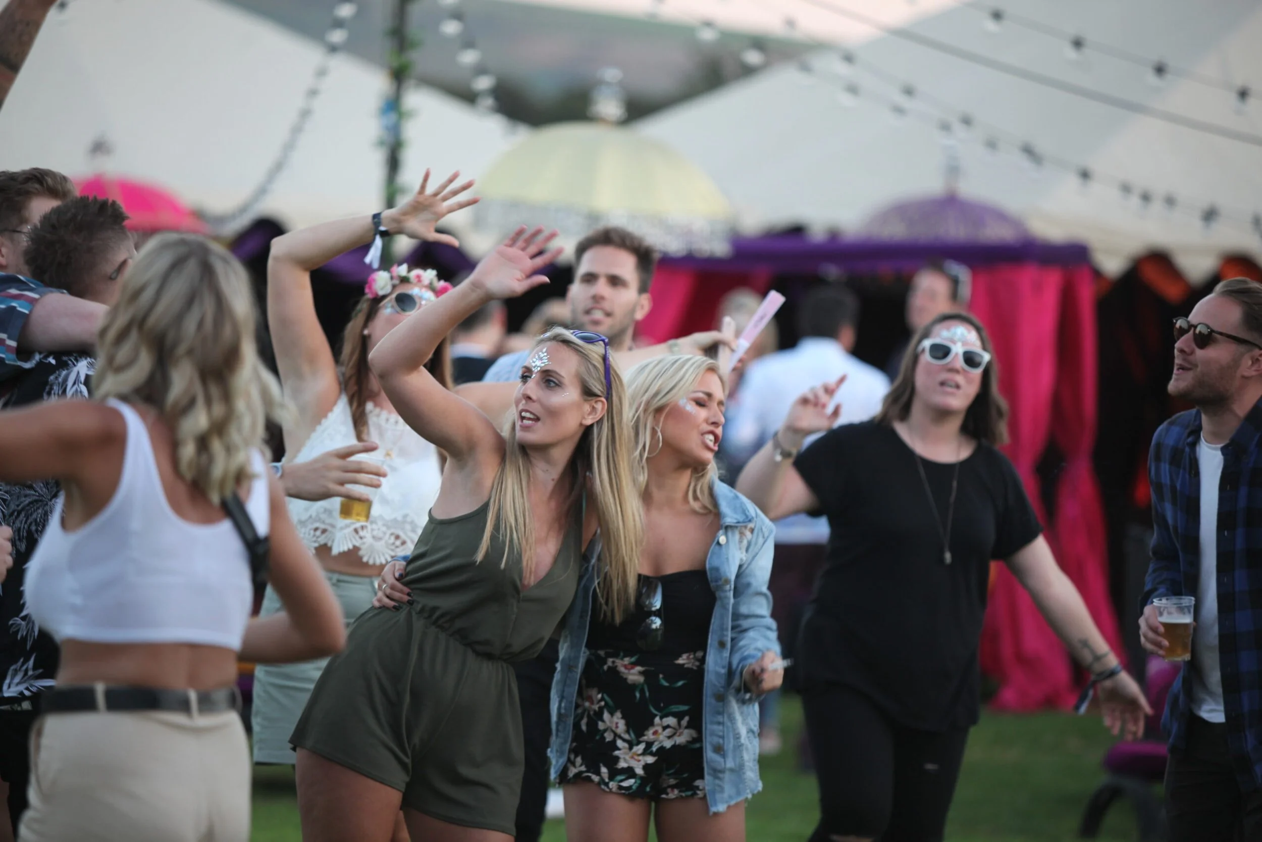 People dancing and enjoying music at an outdoor party or festival with string lights and colorful decorations in the background.