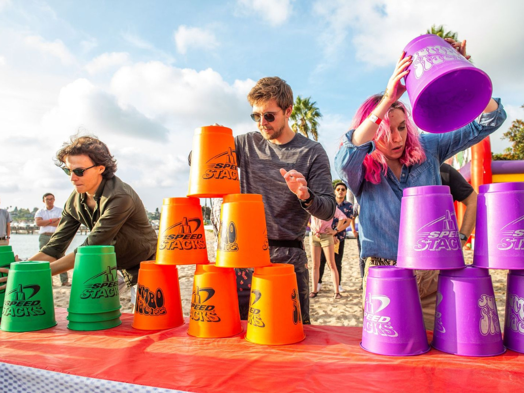 People stacking colorful plastic cups with 'Speed Stacks' logo on a table at the beach.