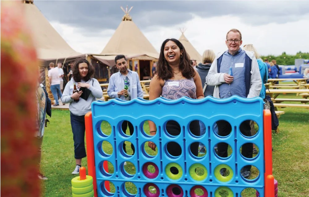 People playing giant Connect Four game outdoors with teepees in the background.