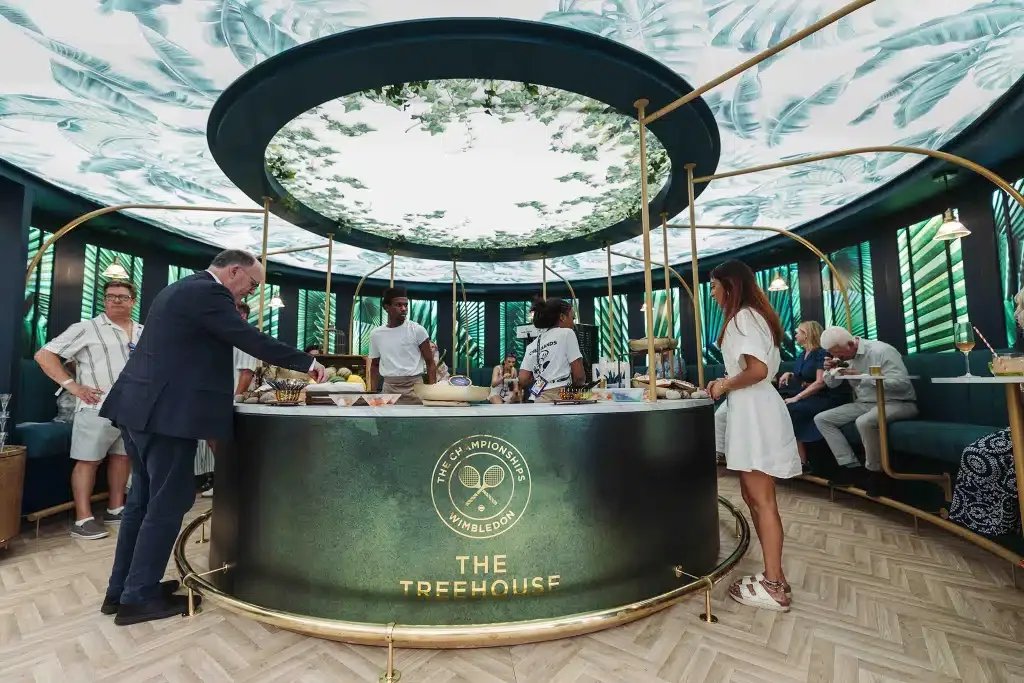 People at a bar called The Treehouse, featuring a lush green tropical theme, with a round bar counter and decorative ceiling resembling a tree canopy.
