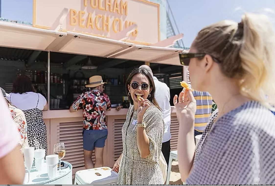 People enjoying food at a beachside food stand with a sign that reads 'FOLLIAM BEACH' in the background.