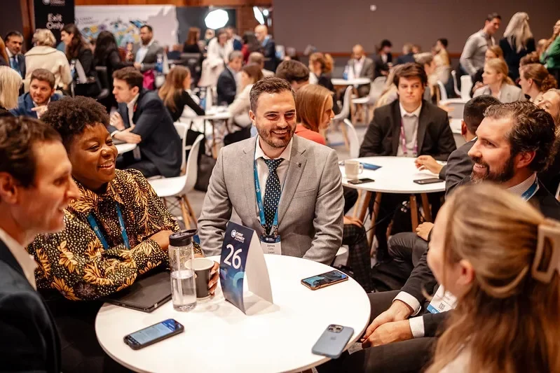 A group of diverse professionals laughing and talking at a round table during a conference or networking event.
