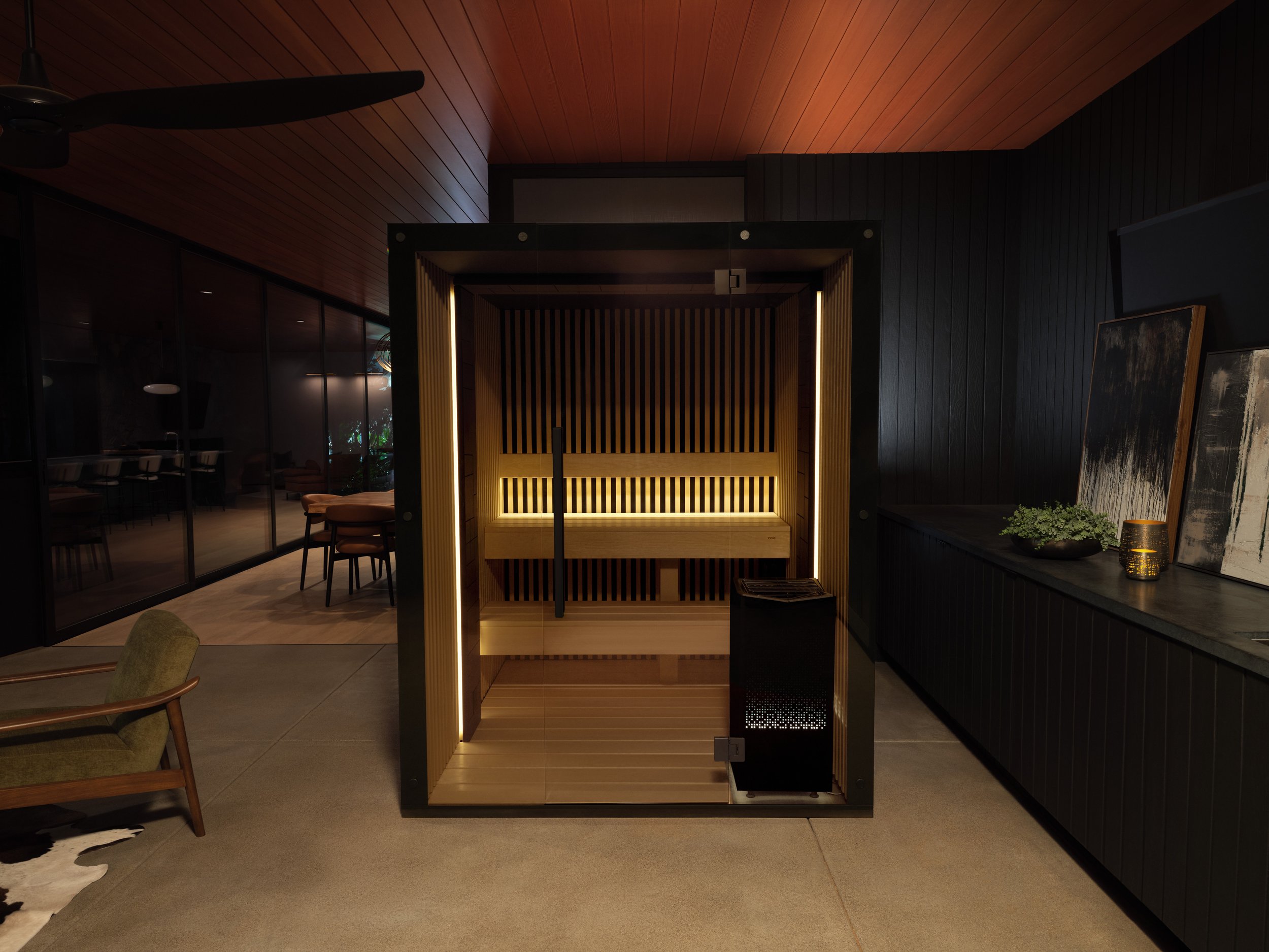 A modern indoor sauna with wooden interior and lighting, situated in a dimly lit room with dark walls and decorative artwork.