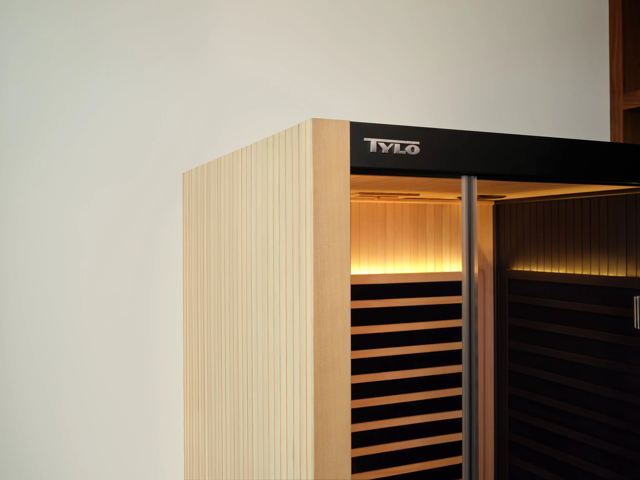 Close-up of a modern heating or cooling unit with the brand name 'TYLO' on the top, showing a sleek design with wood panels and black vents inside.
