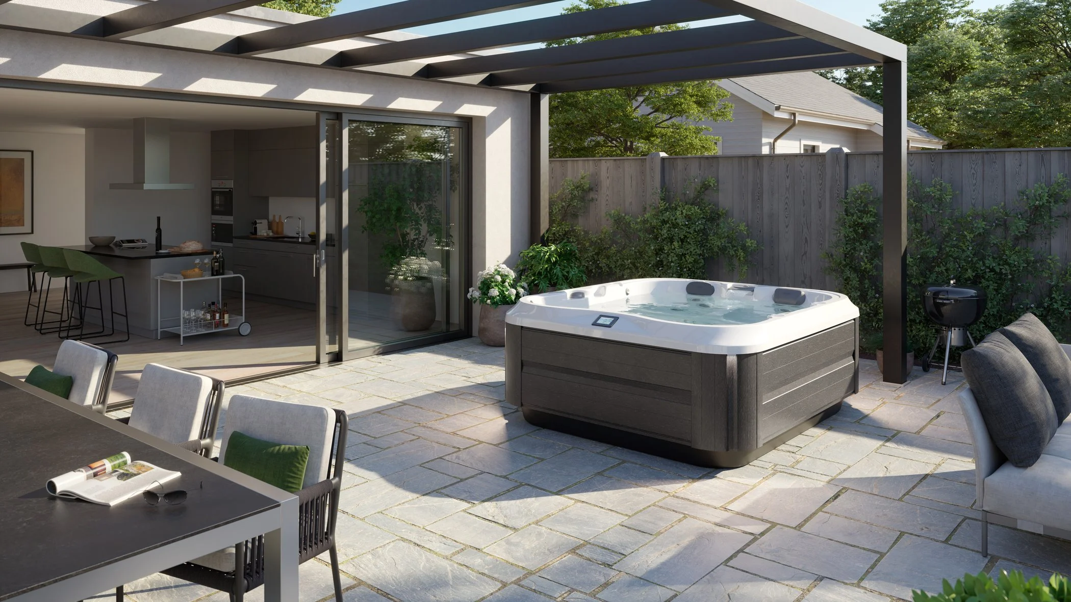 Outdoor patio area with hot tub, dining table with chairs, kitchen in the background, grill to the right, and greenery along the fence.