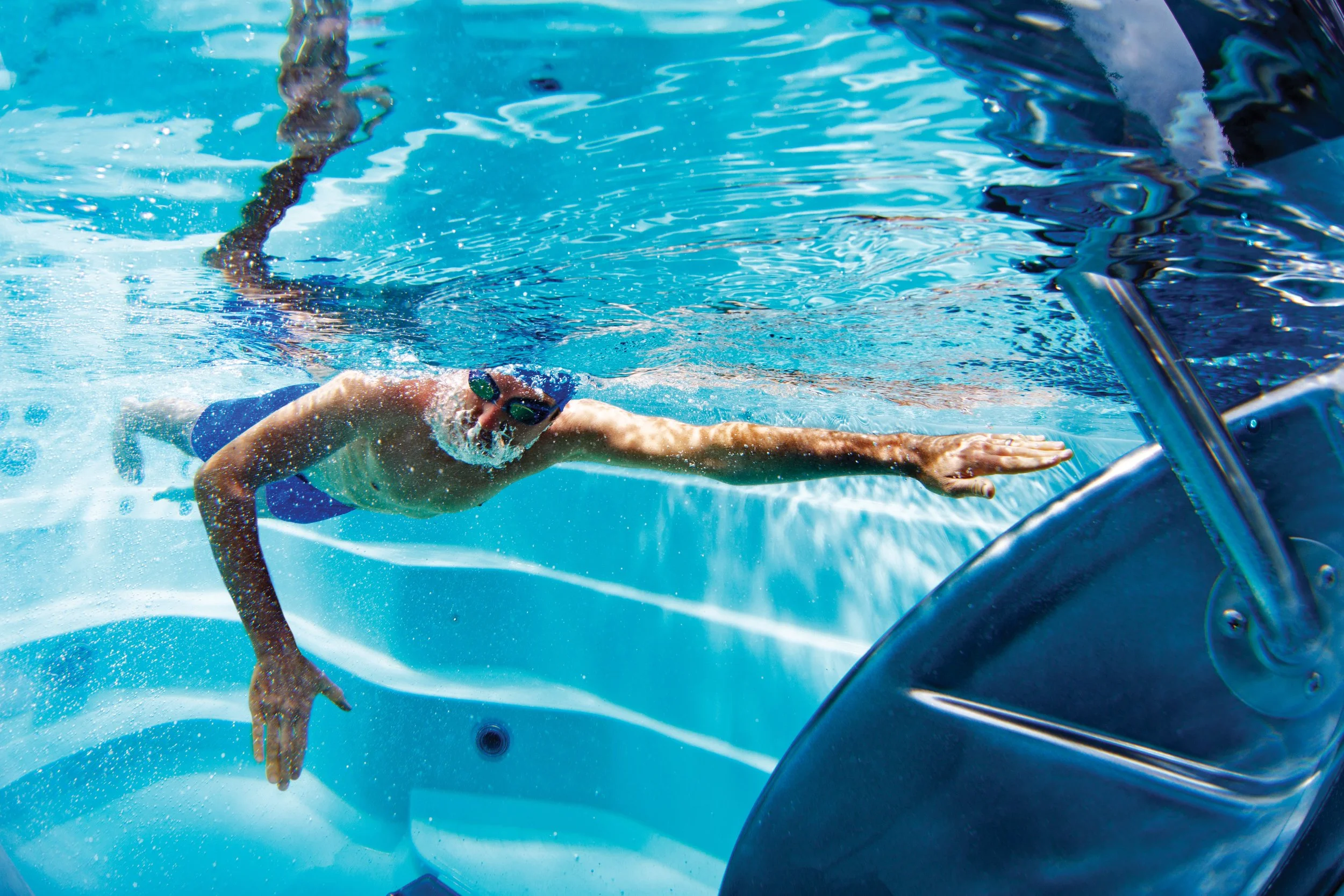 A swimmer in goggles and a swimsuit swimming underwater against the endless pool swim machine current.