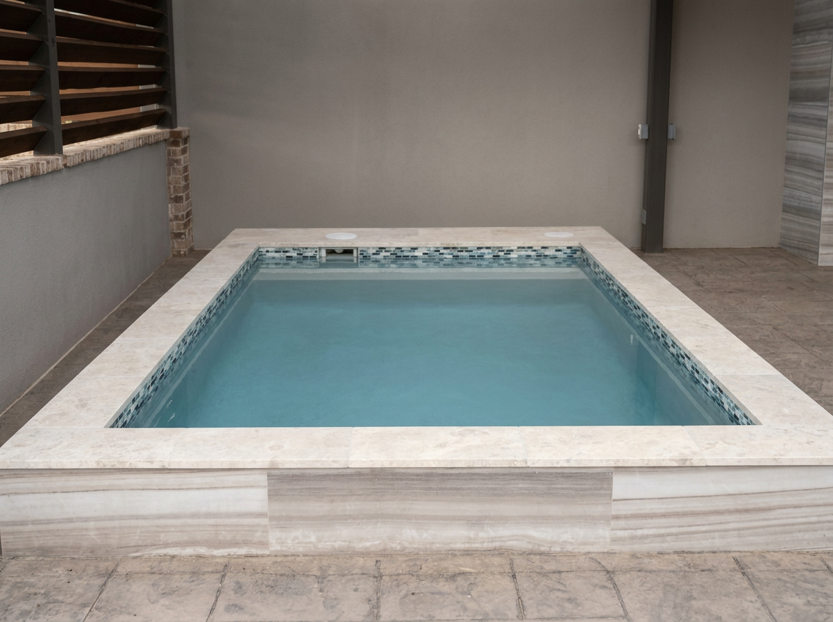 A small above-ground pool with light-colored stone tiles around it, set in a patio area with gray walls and wooden fence panels.