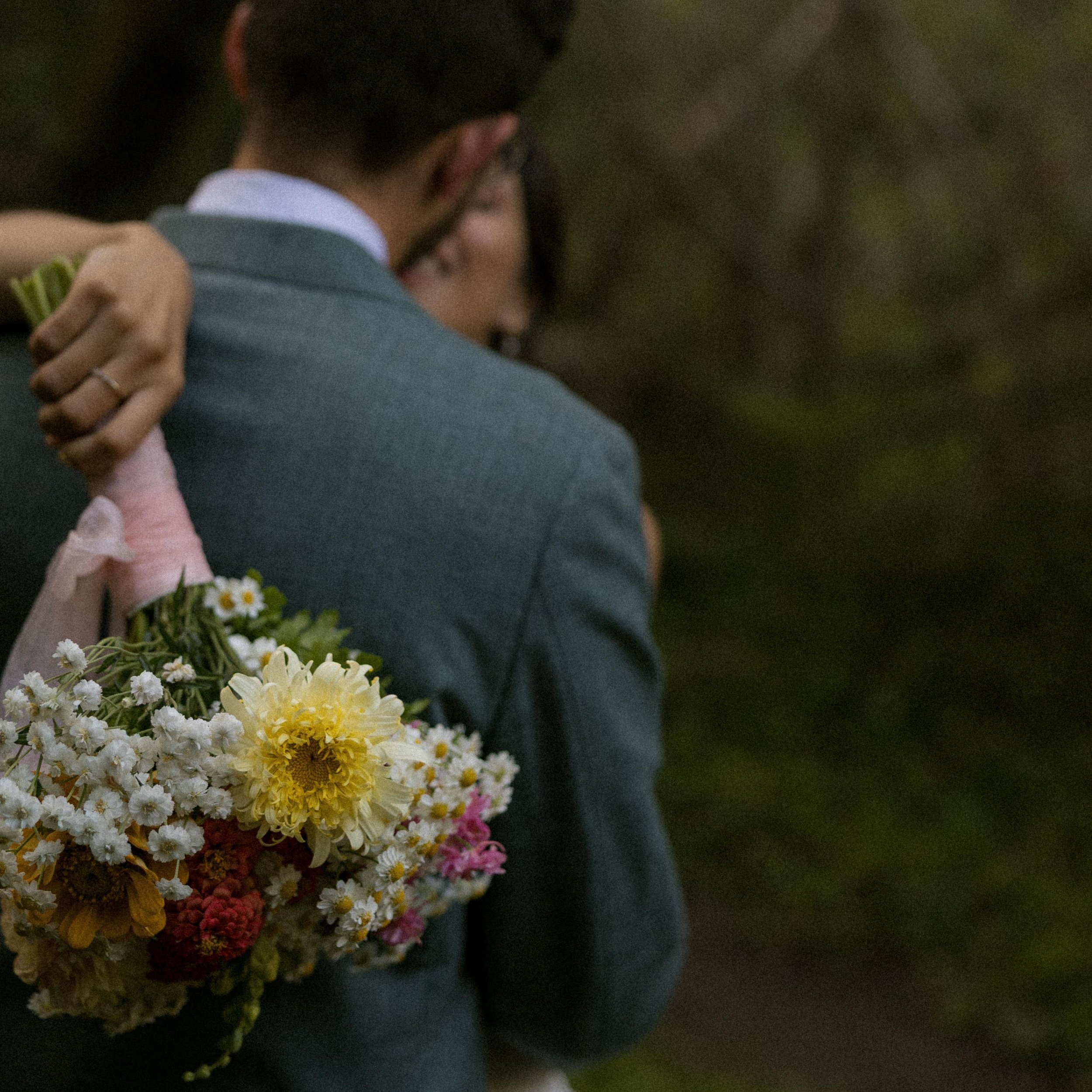 Close-up of a couple embracing, with a woman holding a bouquet of flowers.