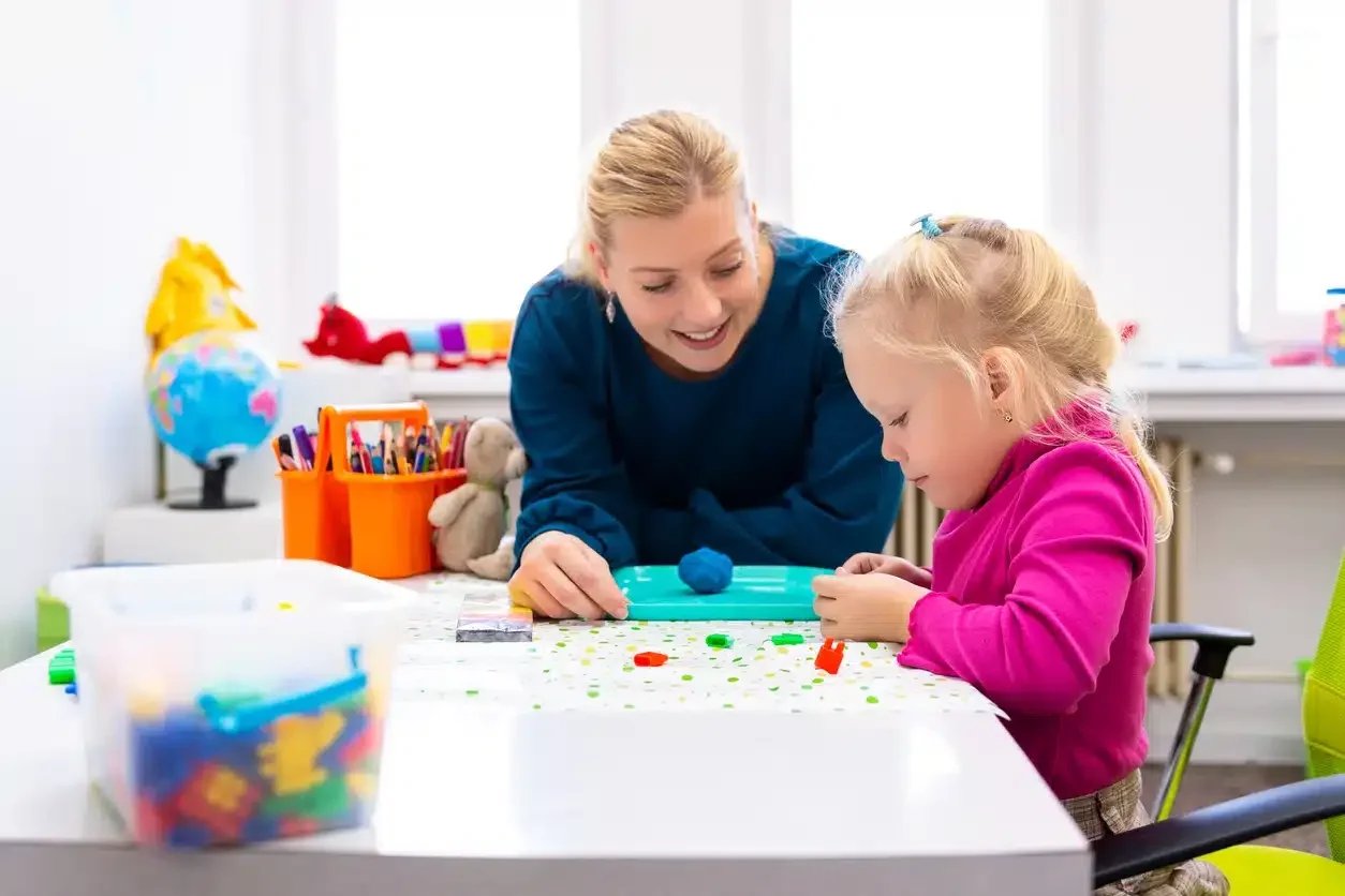 ABA Therapist sitting a table with a young girl while playing with play-doh and working on managing emotions during ABA Therapy in Apollo Beach, FL