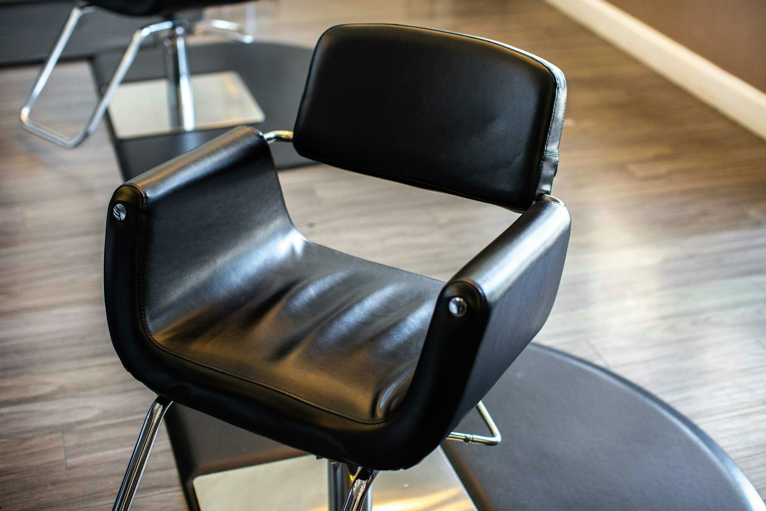 A black modern chair with a swivel base in a room with hardwood floor.