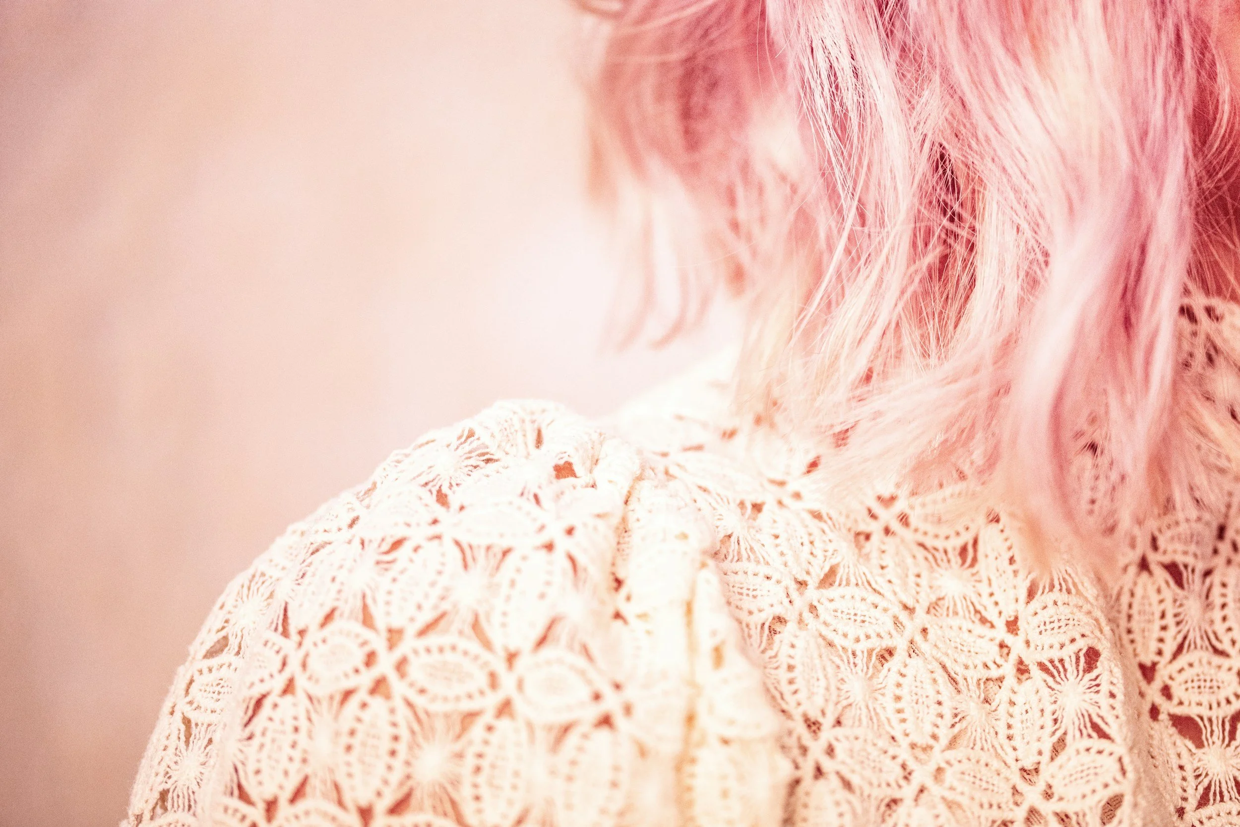 Close-up of a person with pink curly hair wearing a white crochet top.