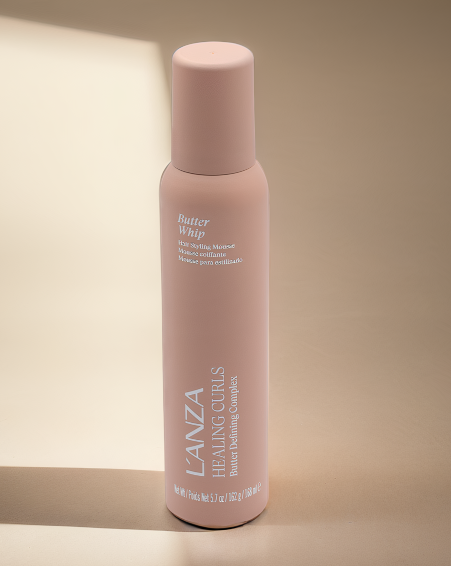 A pink bottle of L'ANZA Healing Gurs Butter Defining Complex hair styling mousse with a smooth cylindrical shape and a matching pink cap.