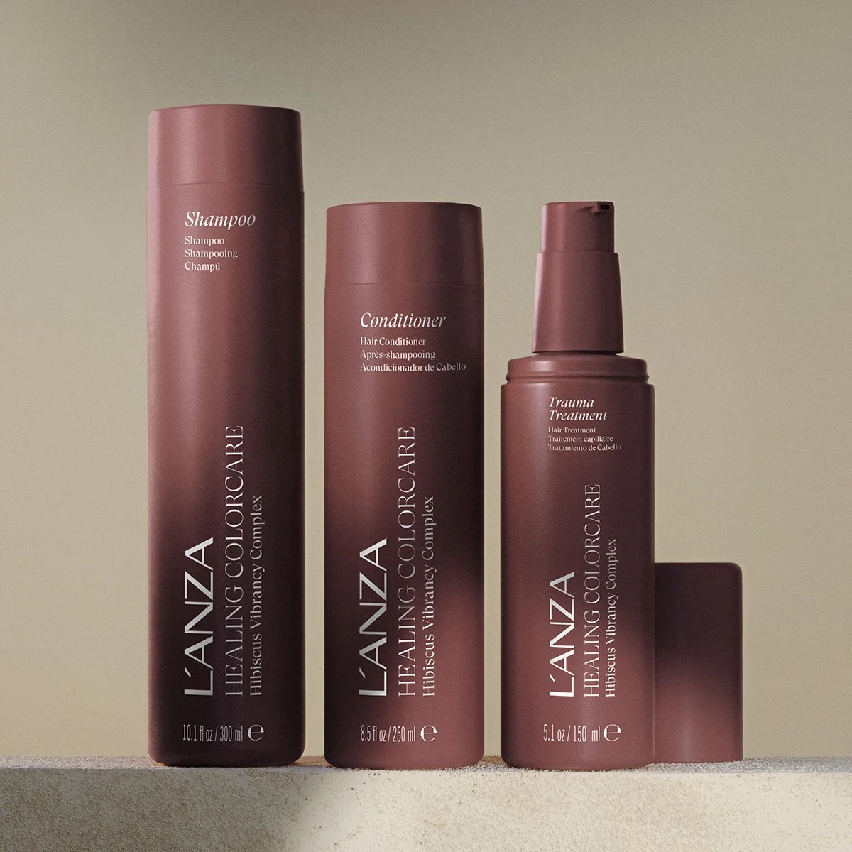 Three hair care bottles labeled Shampoo, Conditioner, and Trauma Treatment from L'ANZA Healing Colorcare, placed on a neutral surface against a plain background.