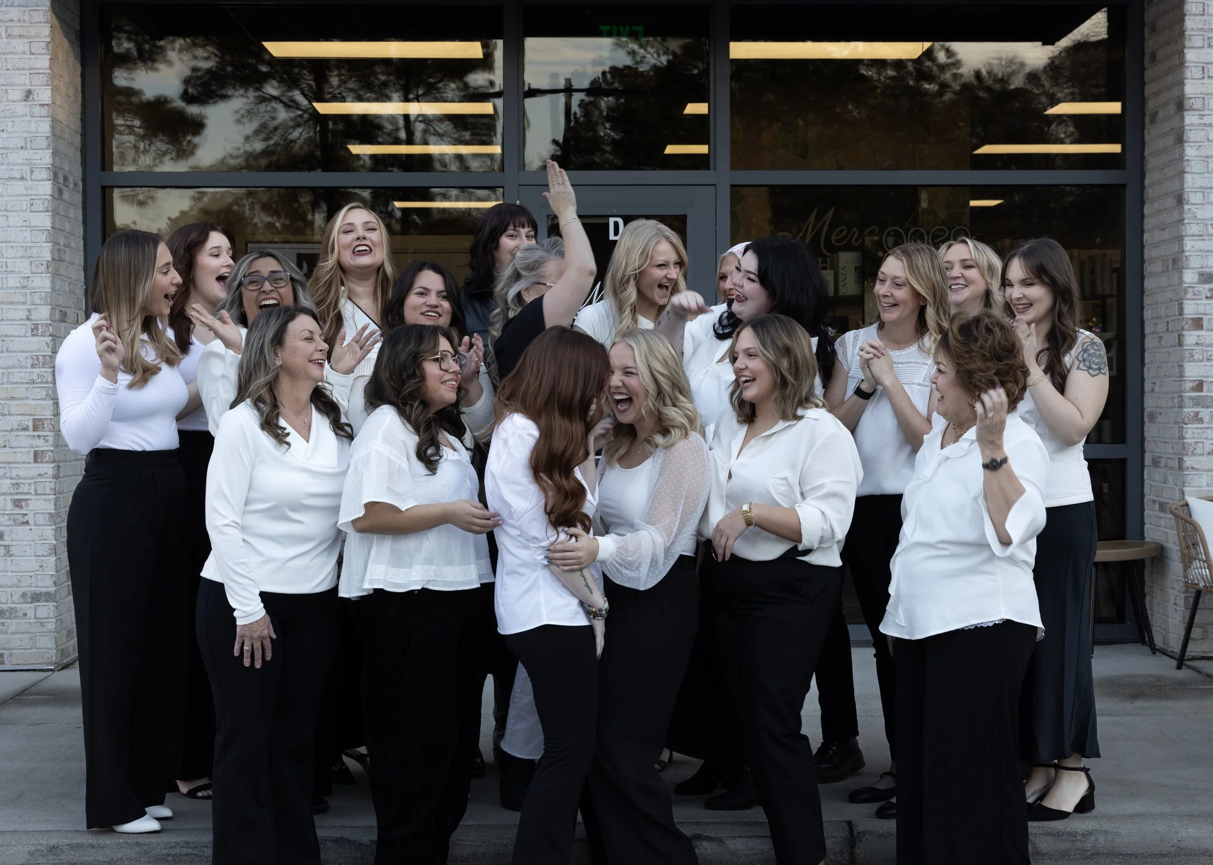 Group of women laughing and celebrating outside a building with glass doors