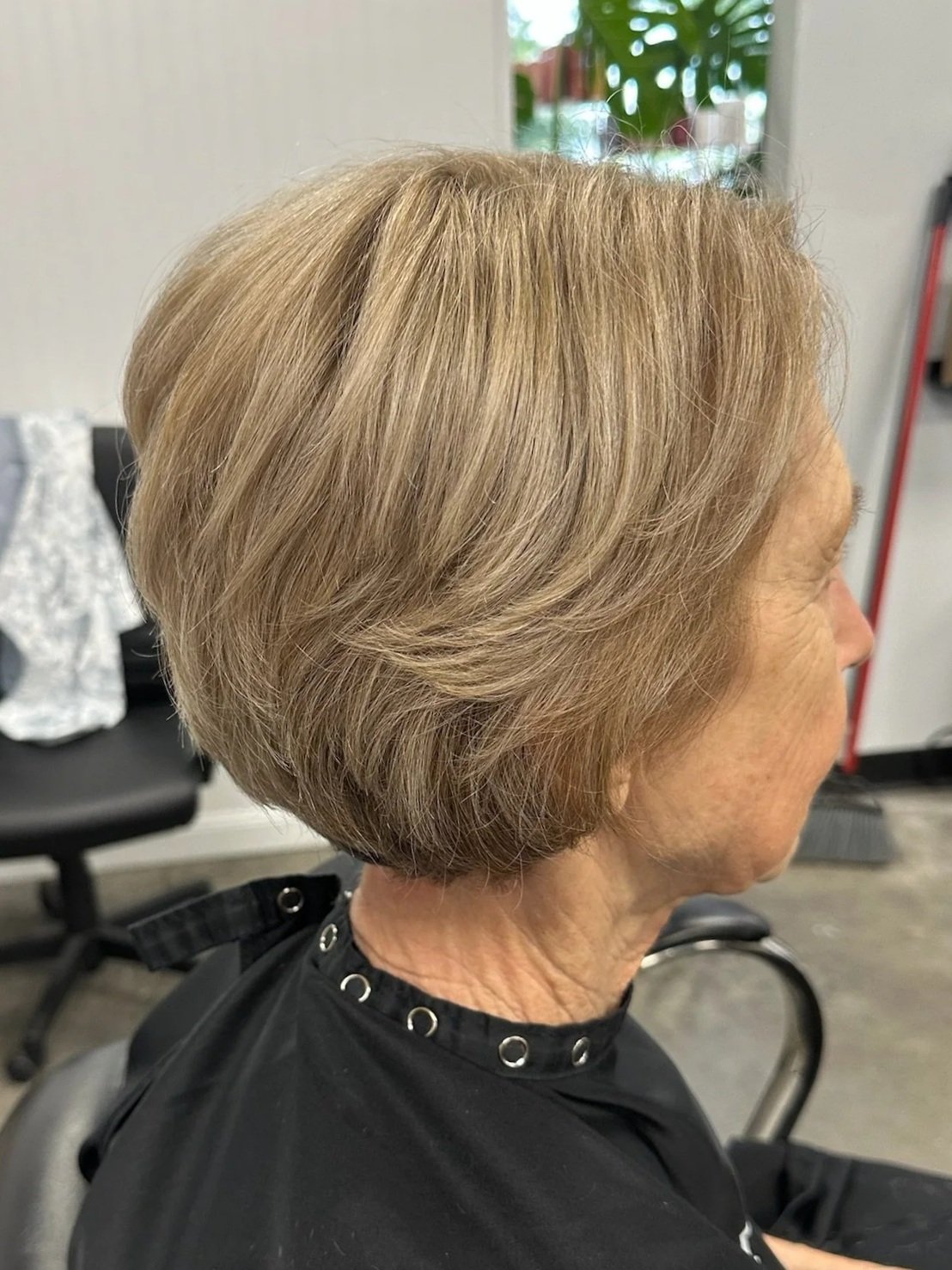 Side view of an elderly woman with short, styled blonde hair, sitting in a salon chair.
