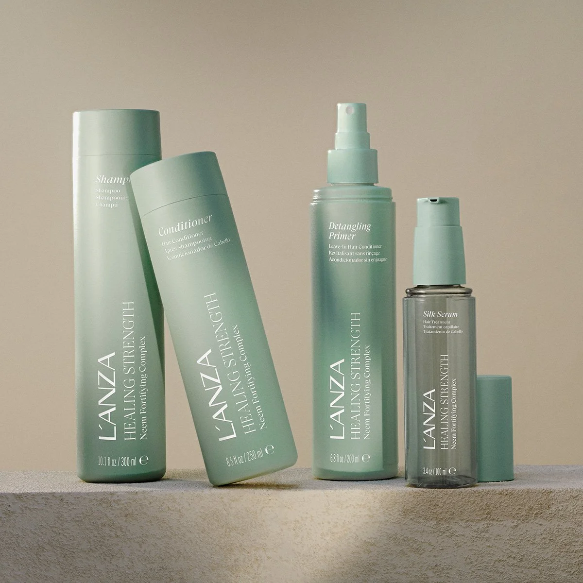 A collection of four teal hair care bottles including shampoo, conditioner, detangling primer, and silk serum, displayed on a textured beige surface against a plain wall.