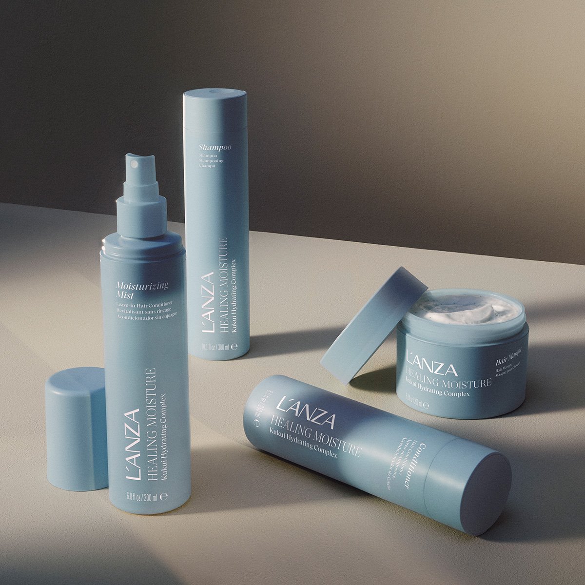 Multiple skincare products from LANZA, including a moisturizing mist, healing moisture spray, and healing moisture cream in blue containers on a beige surface with shadows and neutral background.