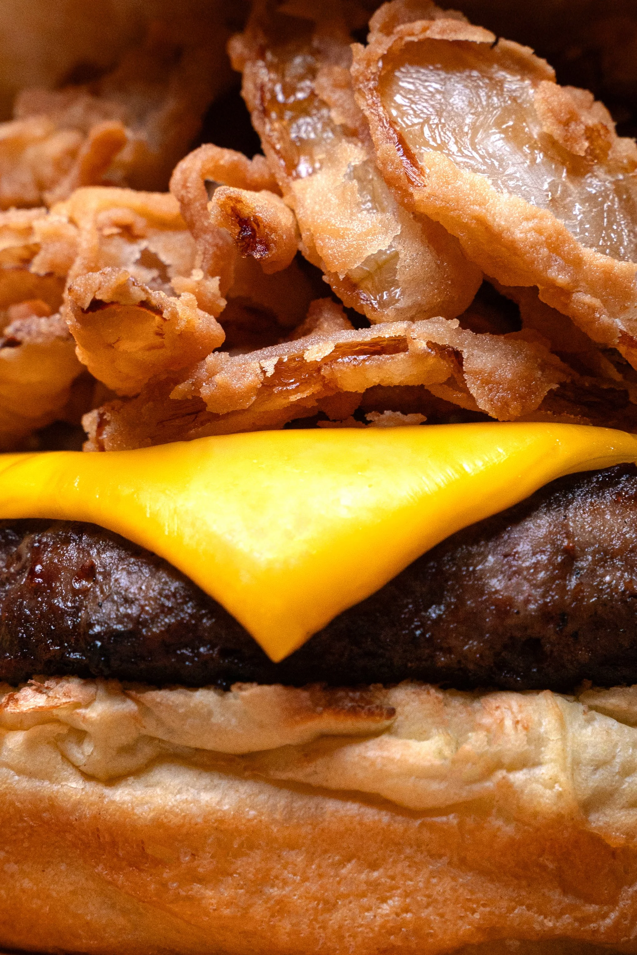 Close-up of a cheeseburger with a beef patty, cheddar cheese, crispy onion rings, and a toasted bun.