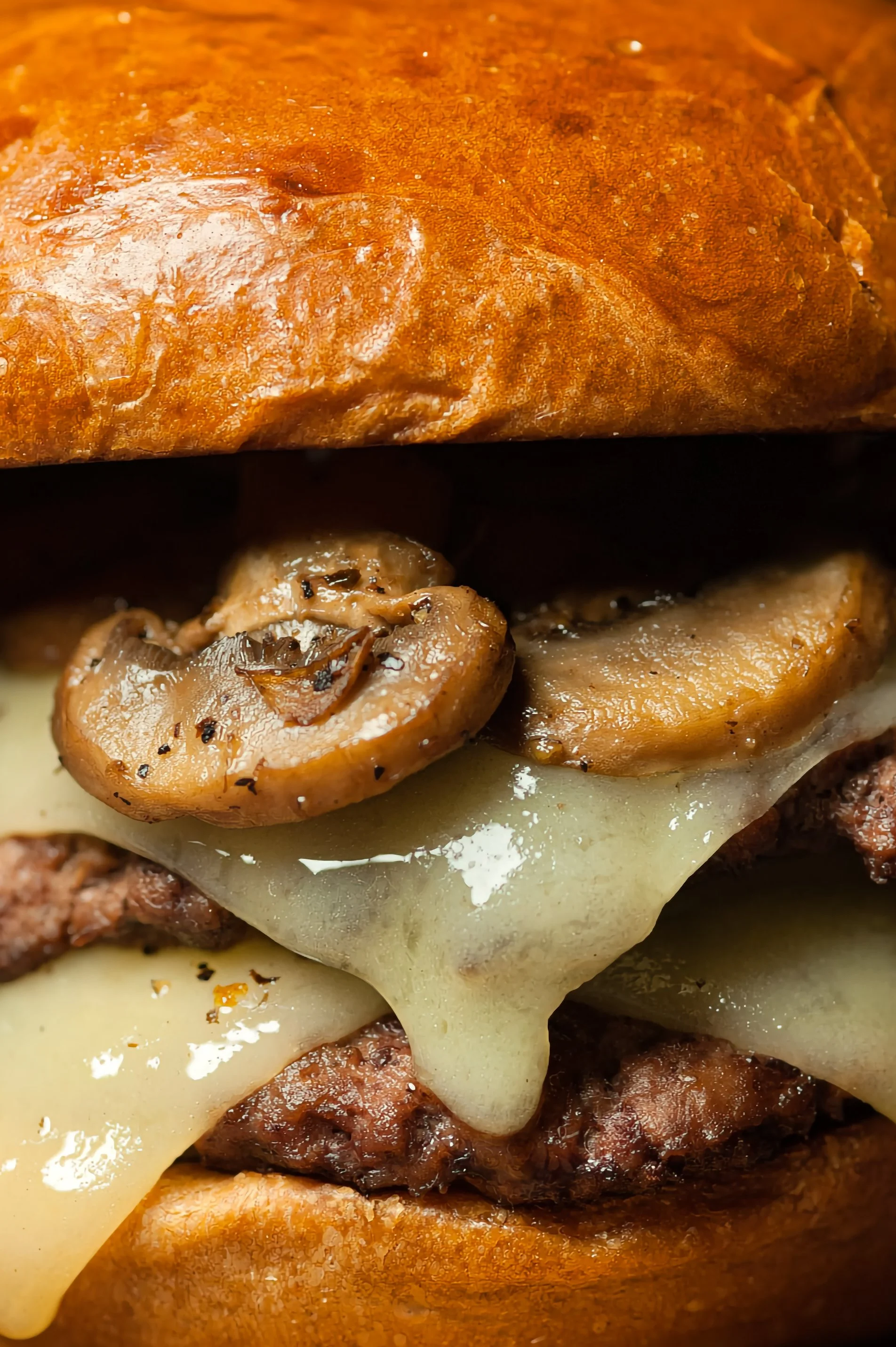 Close-up image of a cheeseburger with mushrooms, melted cheese, and a beef patty in a bun.