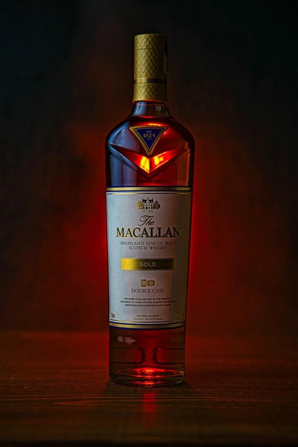 Bottle of The Macallan Gold Highland Single Malt Scotch Whisky with a dark background and warm lighting.
