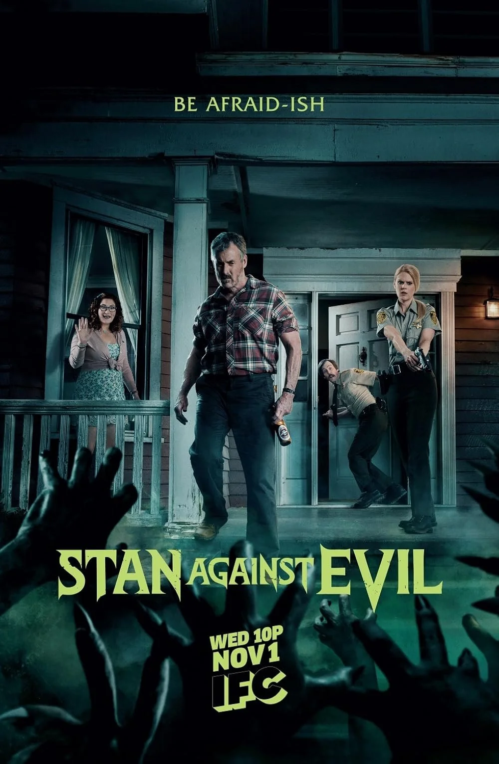 Promotional poster for the show "Stan Against Evil" featuring four people standing outside a house at night with zombie hands reaching in from the bottom.