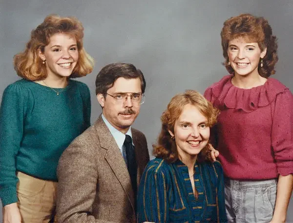Four people, two women and two men, smiling in a studio portrait against a gray background.