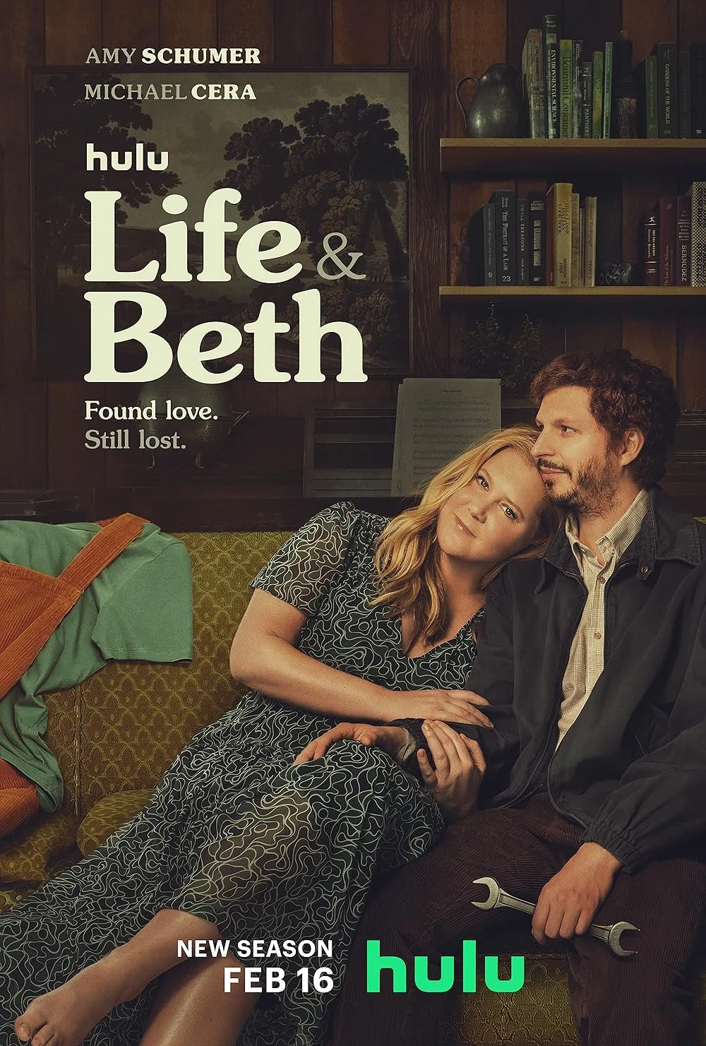 Promotional poster for the Hulu series 'Life & Beth' featuring a woman with blonde hair leaning on a man with dark curly hair, both sitting on a green patterned couch in a cozy room with wooden bookshelves and a large framed picture on the wall.