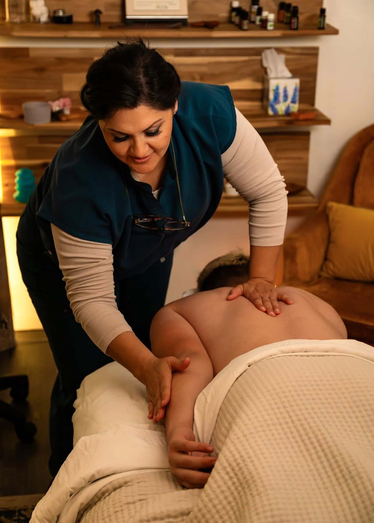 A massage therapist gives a back and arm massage to a person lying face down on a table, covered with a white blanket.